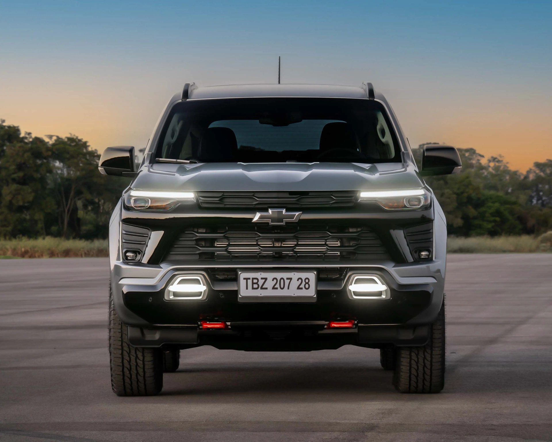 Front view of a silver Chevrolet SUV with LED headlights and daytime running lights on a paved road at sunset.