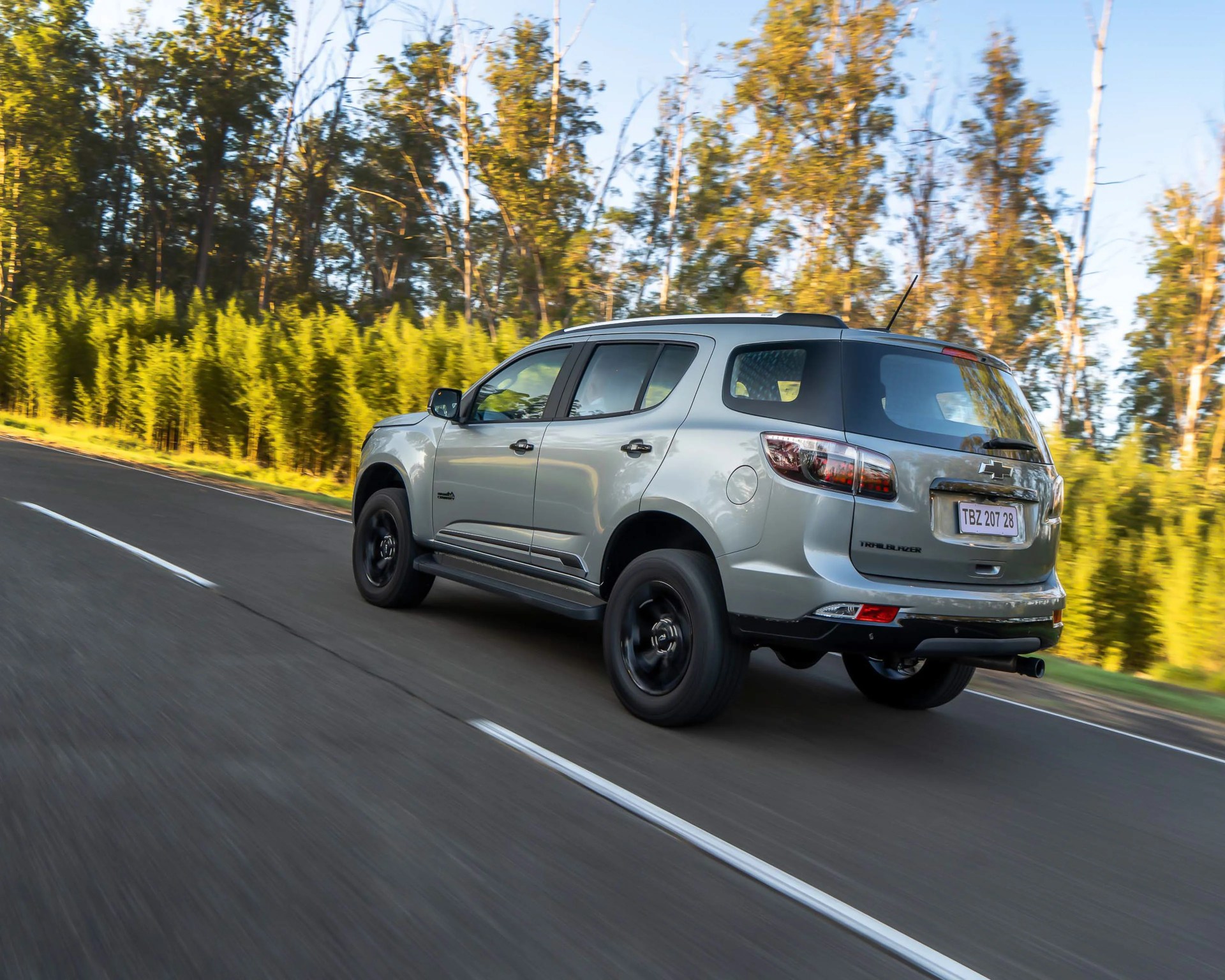 Silver Chevrolet Trailblazer SUV driving on a road with green trees in the background.