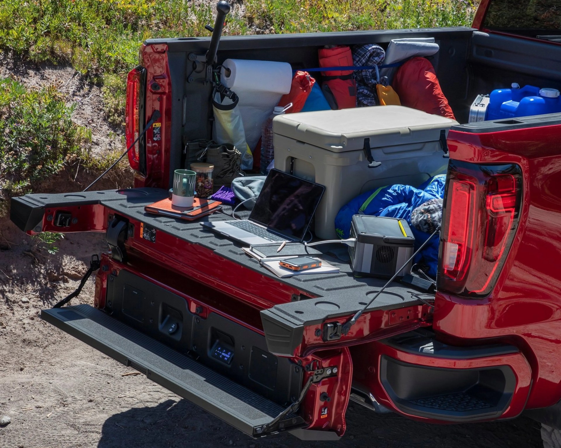 Open red pickup truck bed loaded with camping gear, cooler, laptop, water containers, and paper towels.