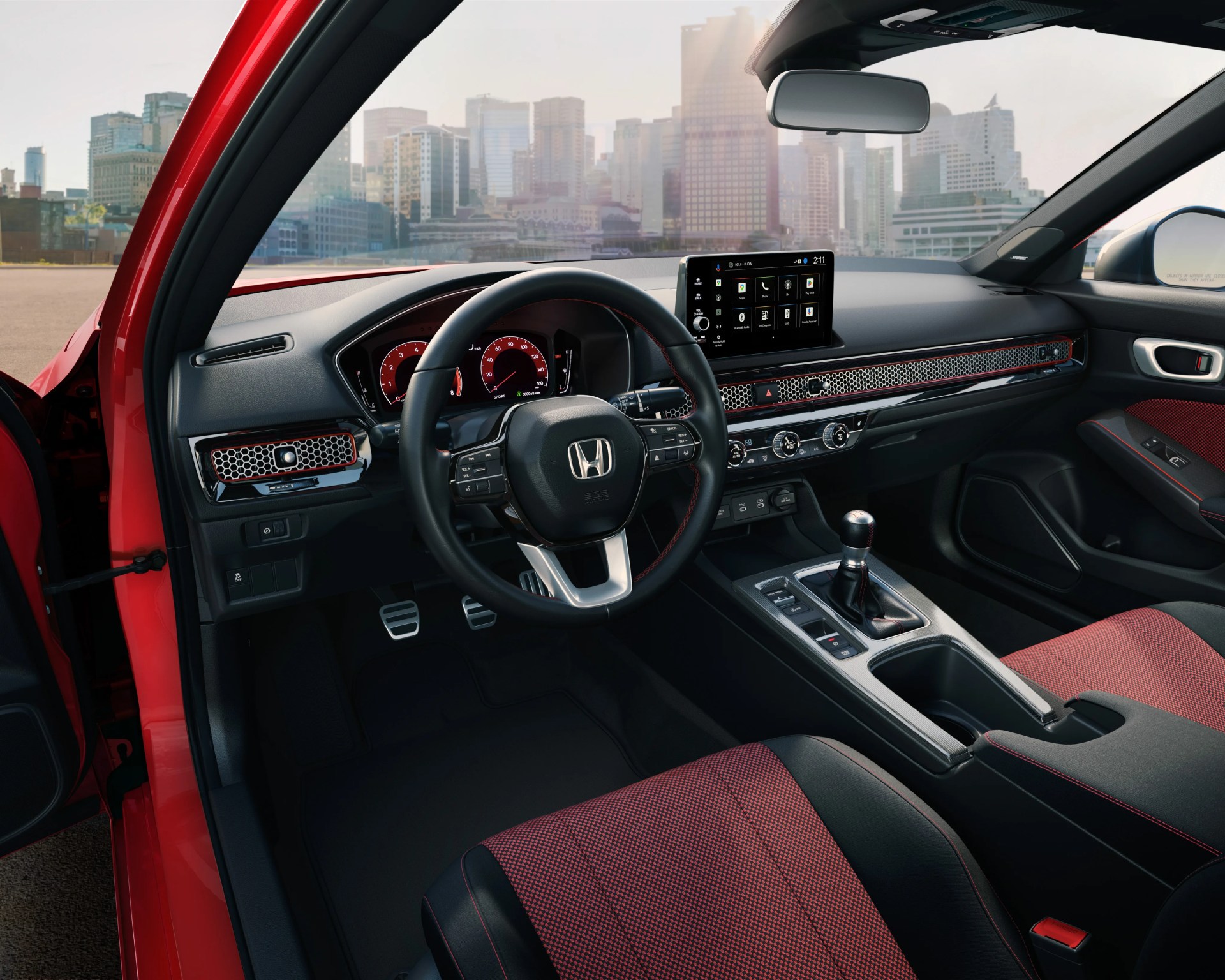 Black and red fabric car seats with black leather steering wheel and digital dashboard in a red car interior.