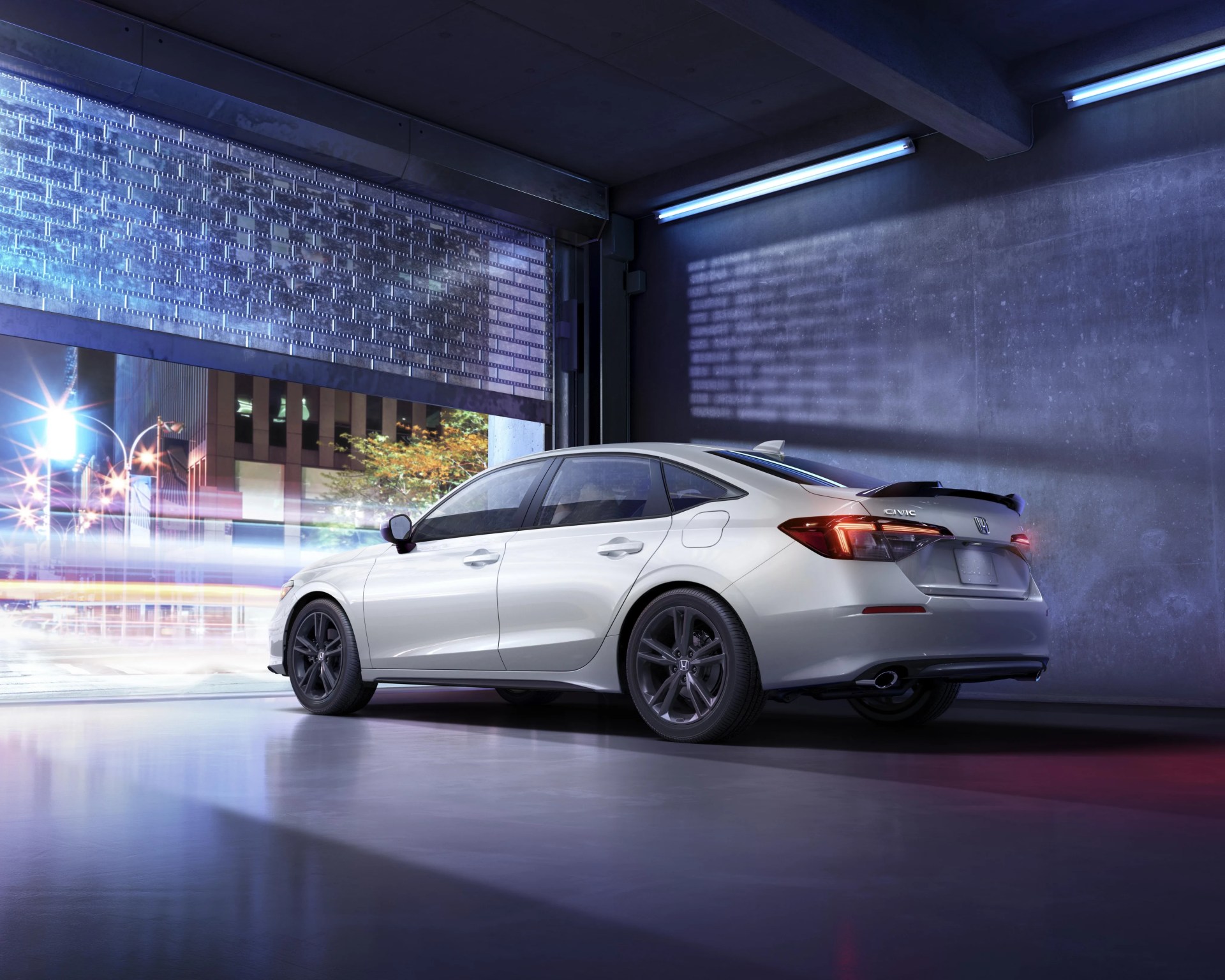 Silver Honda Civic sedan with black wheels parked inside a garage with a partially open metal door.