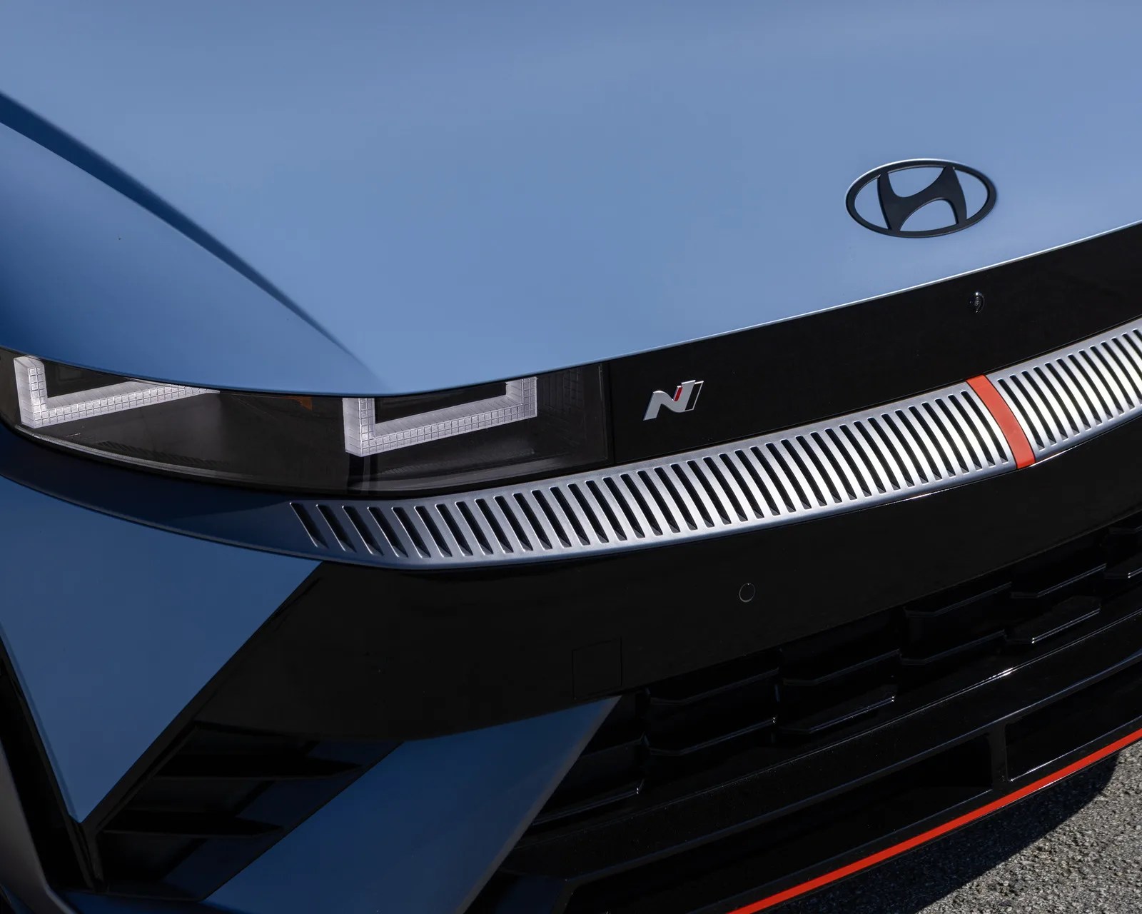Close-up of a blue Hyundai car front with black grille, silver vent trim with red accent, and LED headlights.