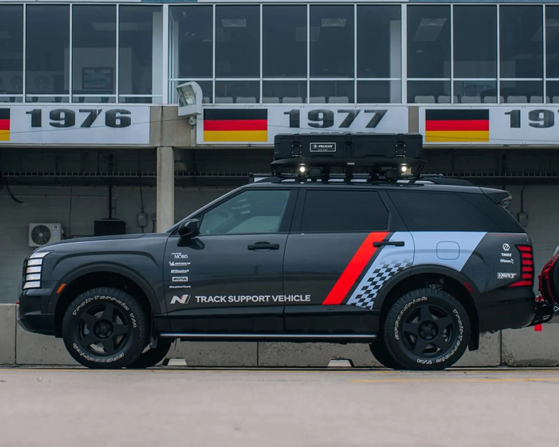Black SUV with roof-mounted Pelican case and "N Track Support Vehicle" decal on the side, parked in front of a building.