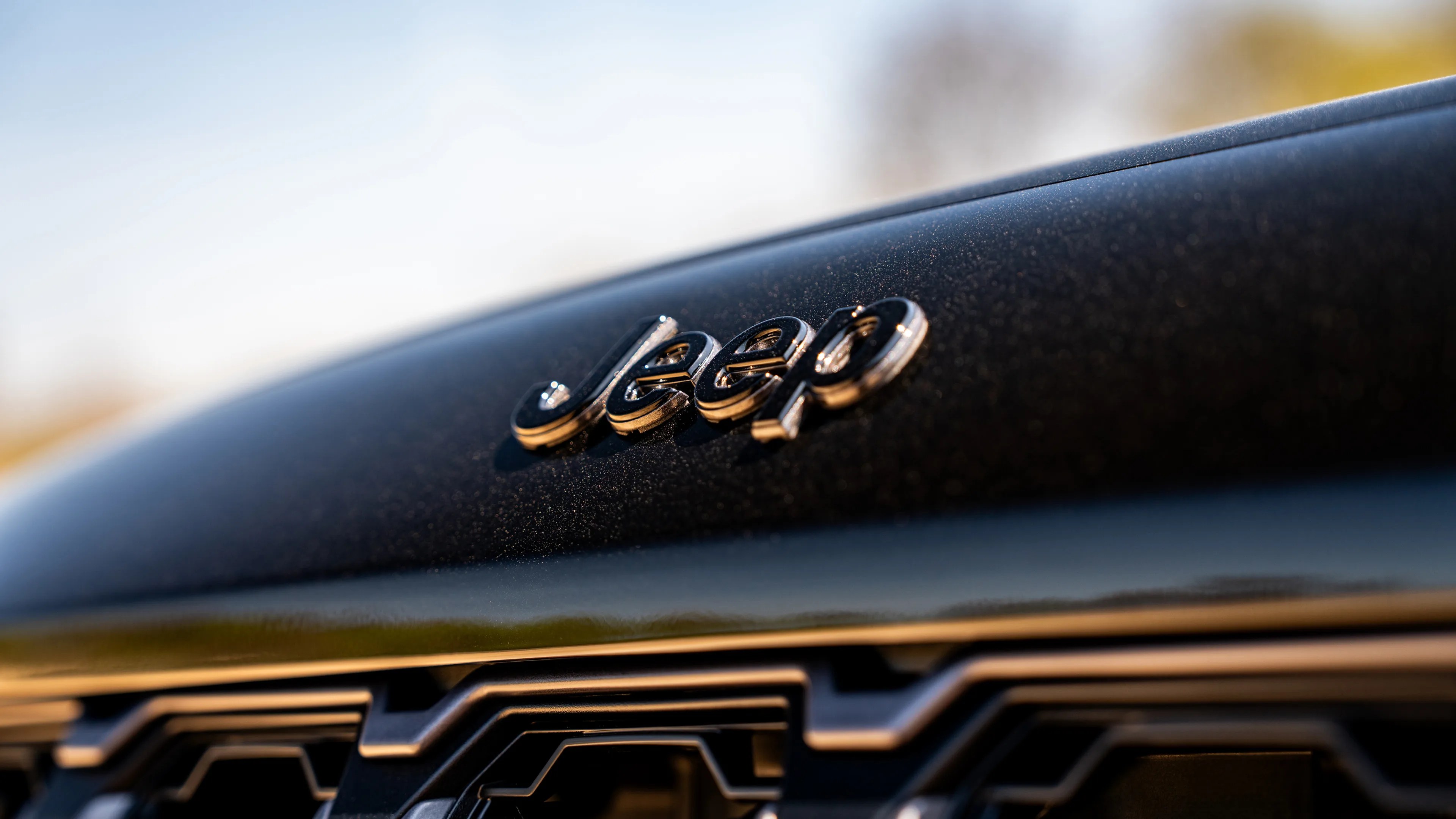 Close-up of a black Jeep vehicle hood with a shiny Jeep logo and part of the front grille visible.