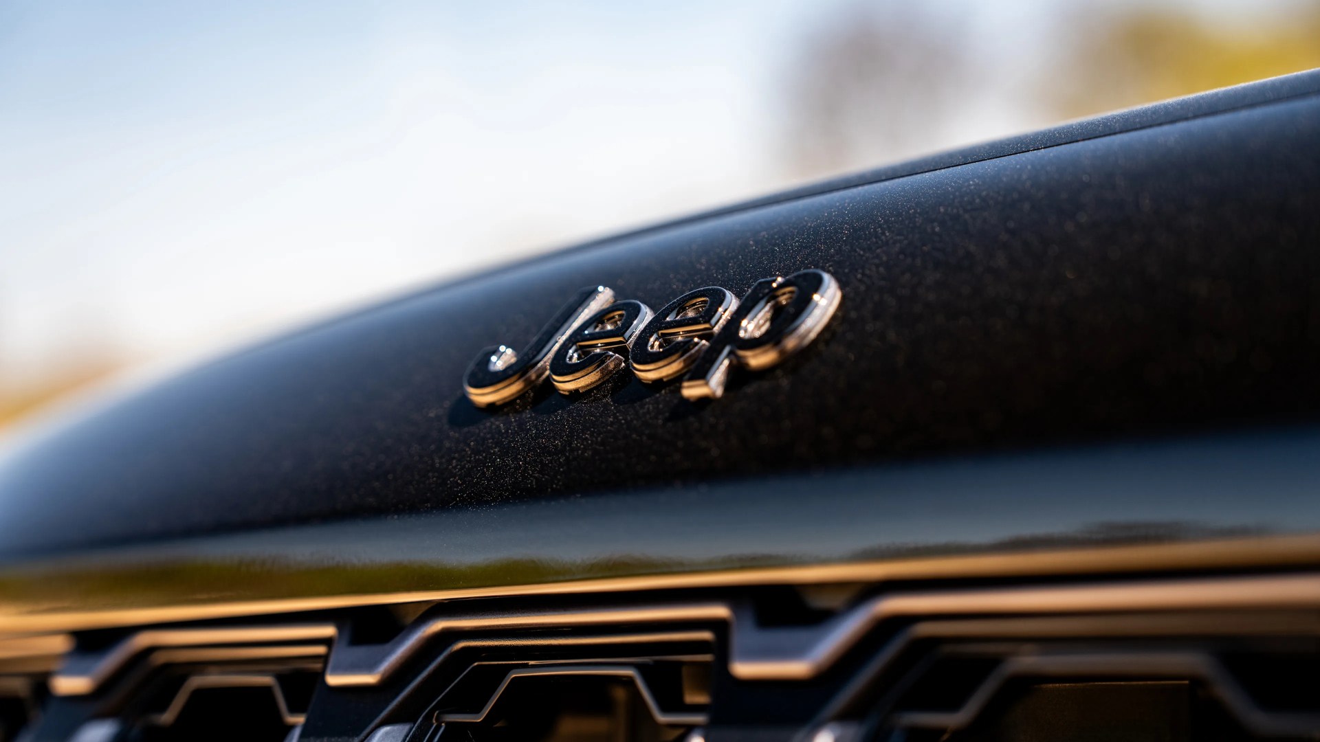 Close-up of a black Jeep vehicle hood with a shiny Jeep logo and part of the front grille visible.