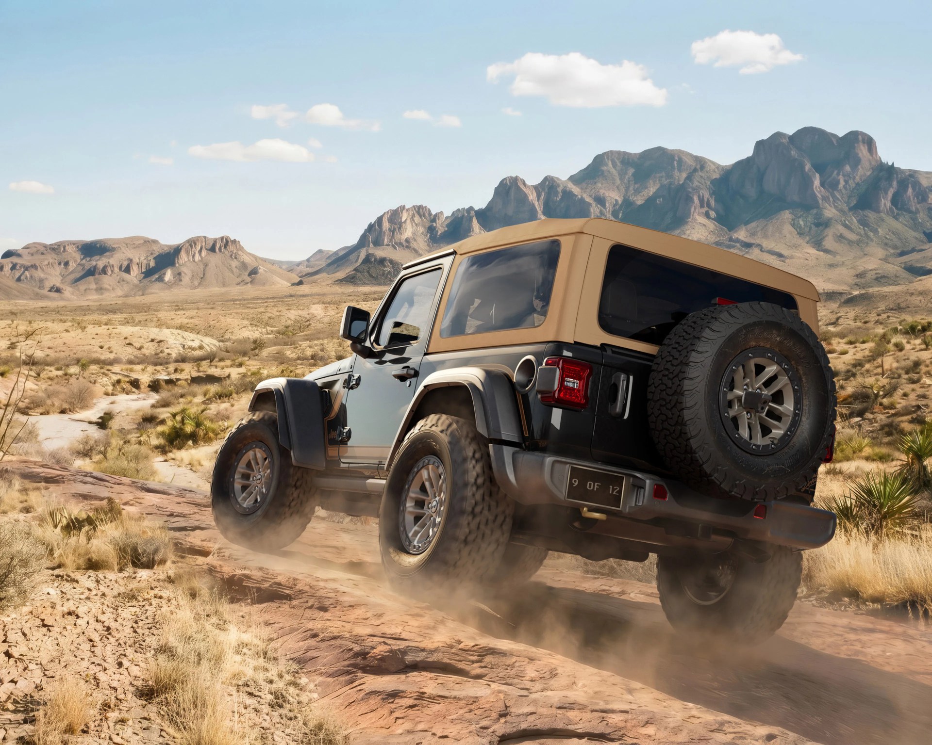 Black Jeep Wrangler with tan soft top driving on rocky desert terrain with mountains in the background.