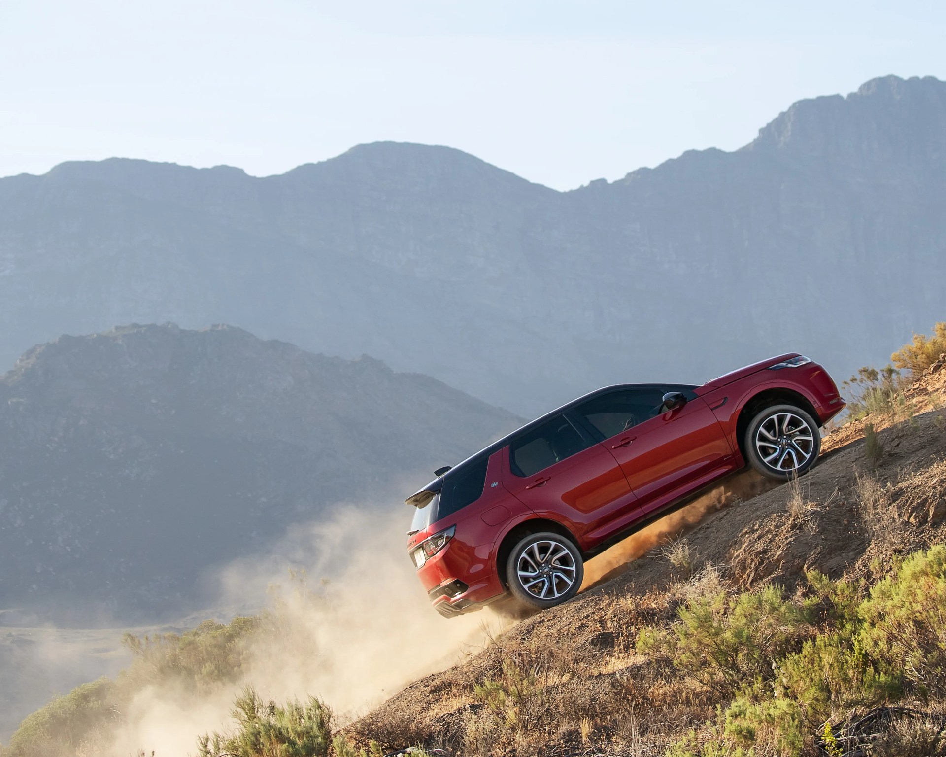 Red SUV climbing a steep dusty hill with mountains in the background.