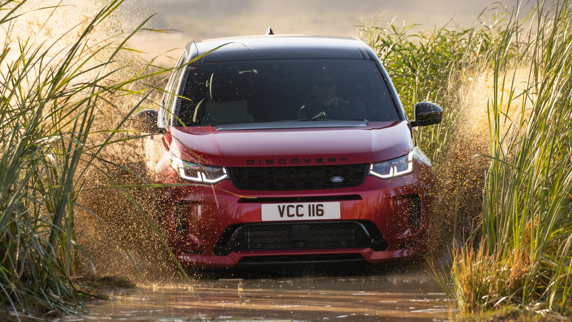 Land Rover Discovery Sport kırmızı SUV su birikintisinden geçerken