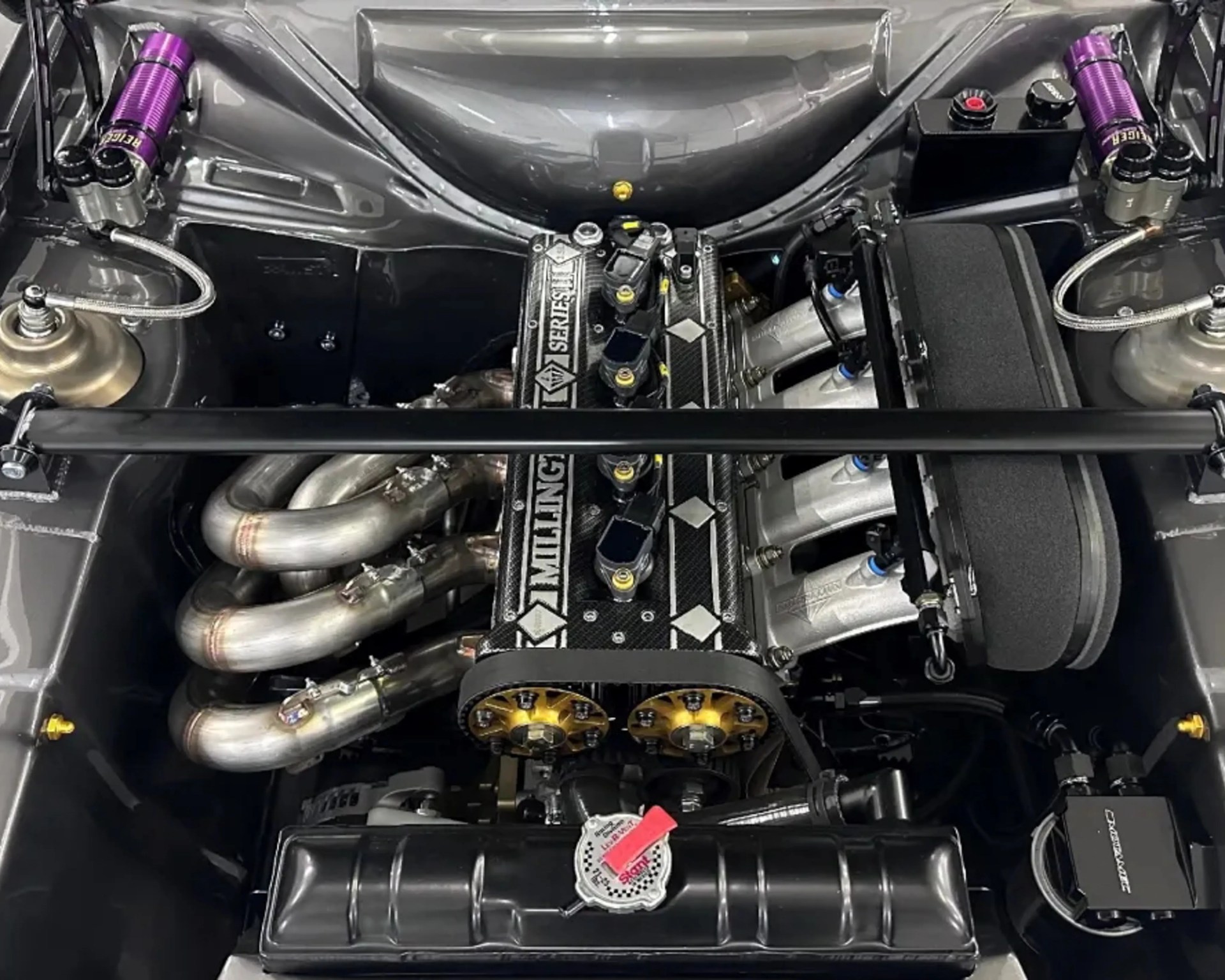 High-performance car engine with Emmilling Series 1 carbon fiber valve cover and purple coilovers.
