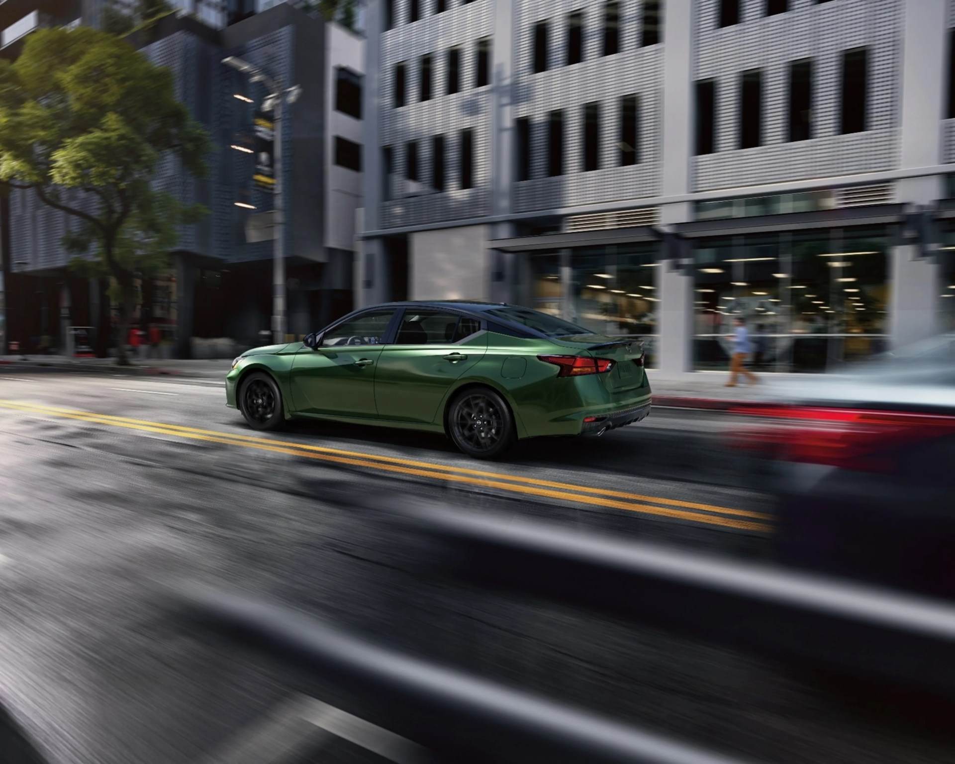 Green sedan with black roof driving on a city street past modern buildings.