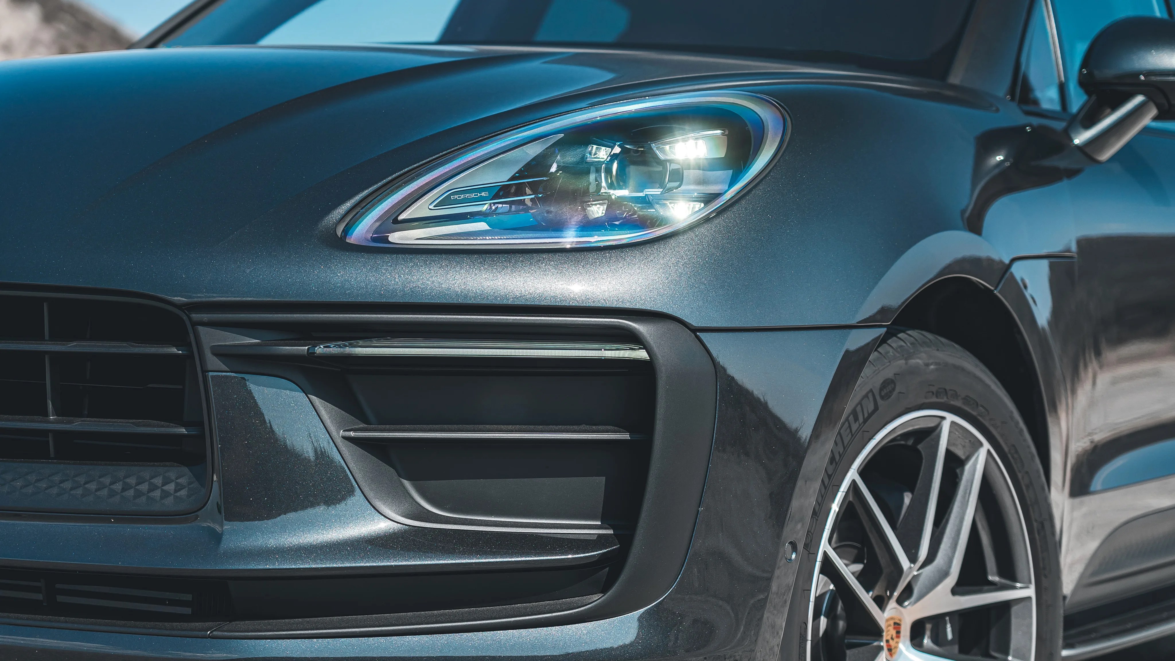 Close-up of a dark metallic Porsche front headlight and wheel with Michelin tire.
