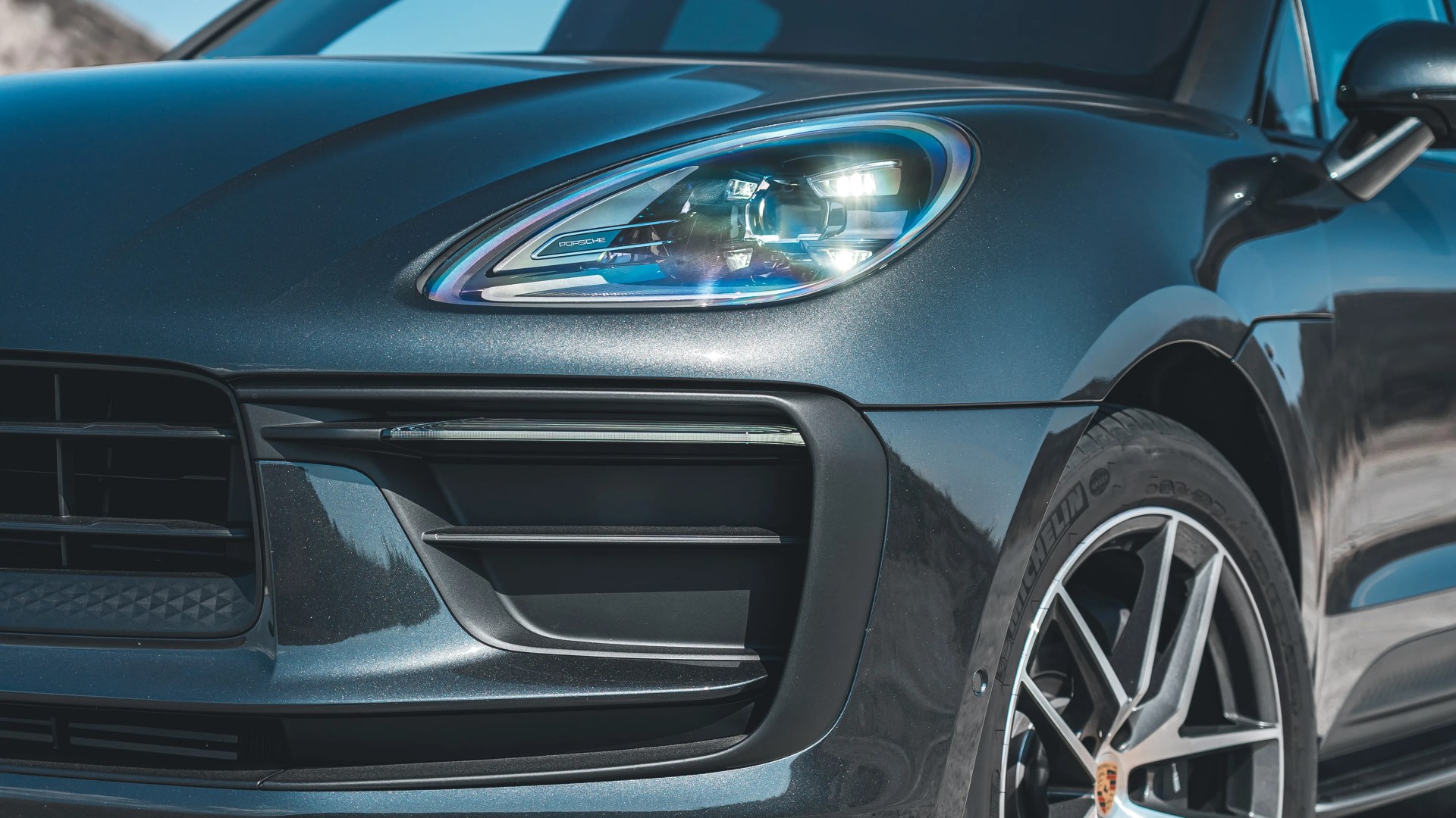 Close-up of a dark metallic Porsche front headlight and wheel with Michelin tire.