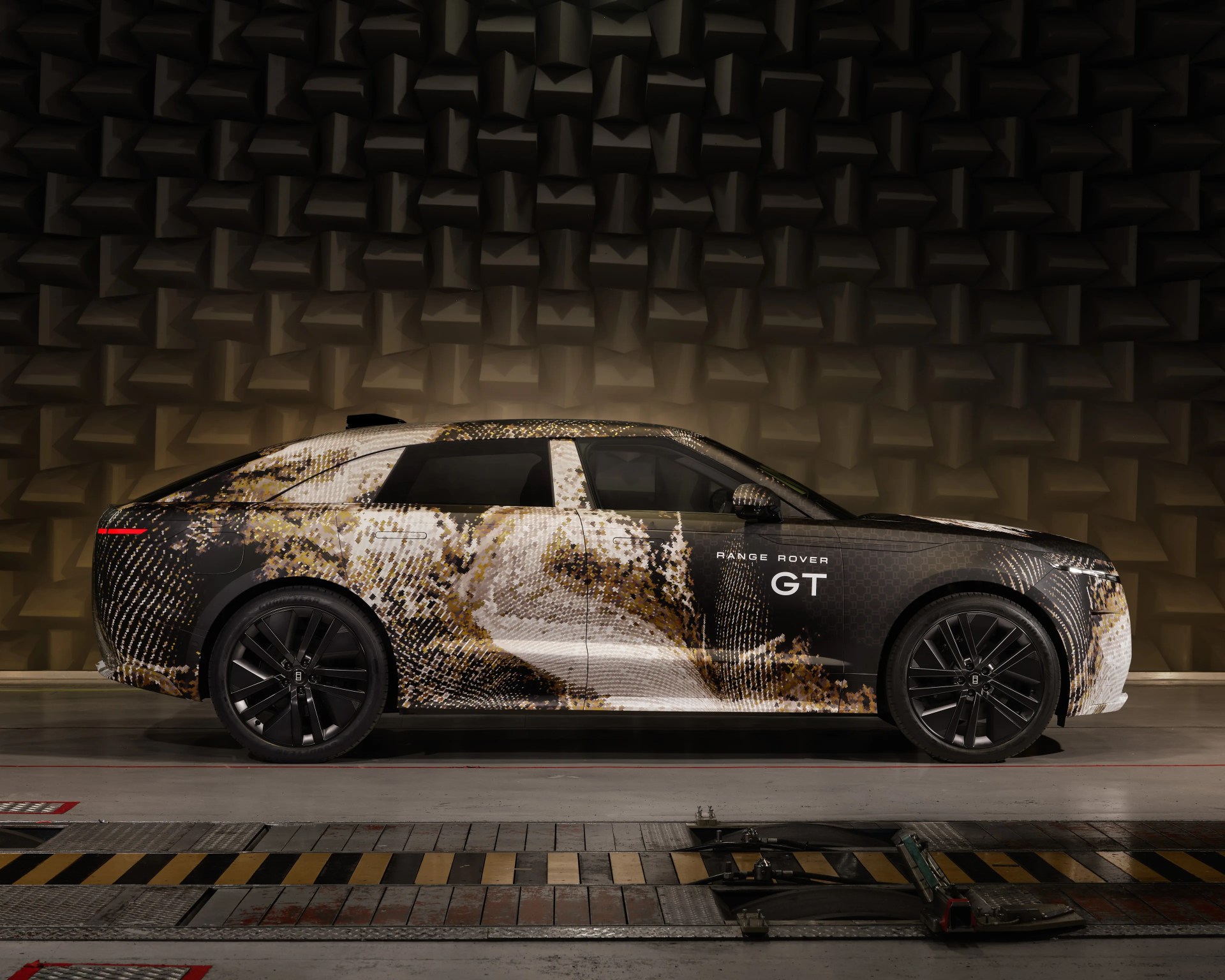 Side view of a Range Rover GT with a pixelated camouflage wrap in a soundproof room.