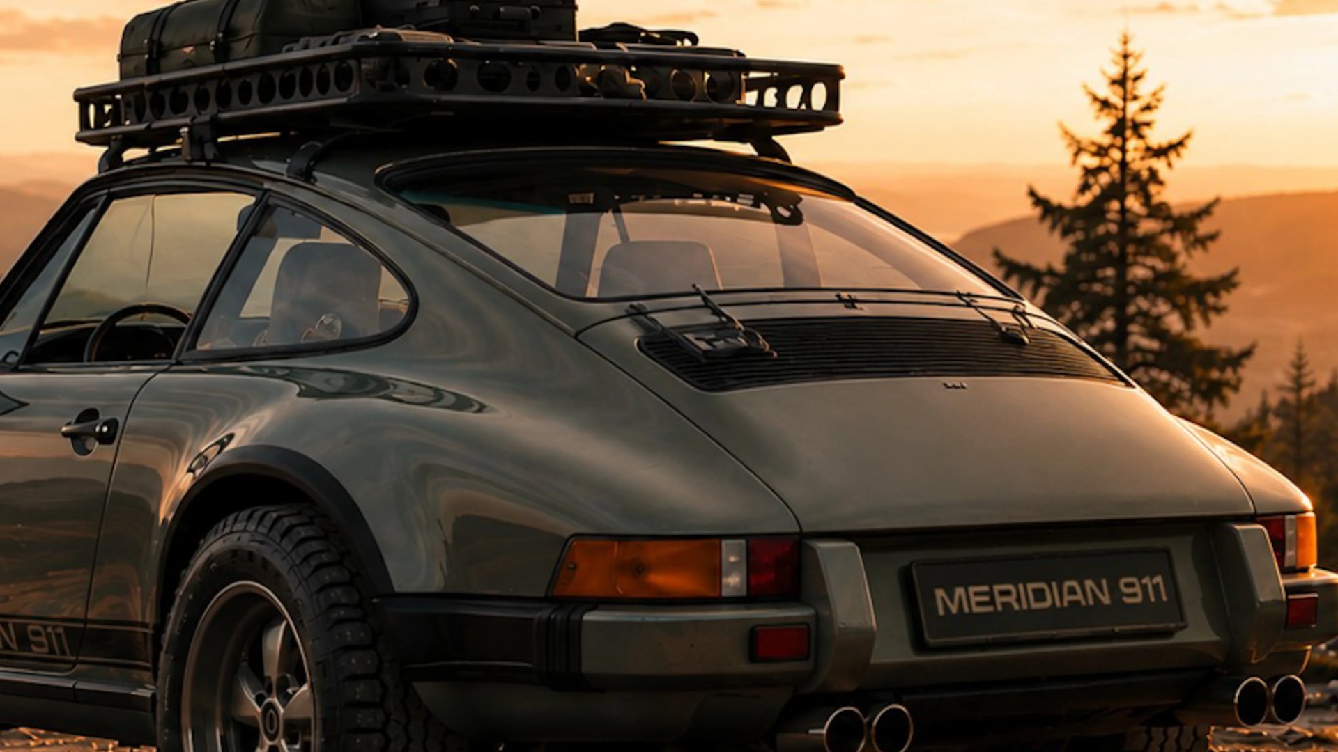 Dark green Porsche 911 with roof rack and luggage at sunset in a mountainous forest setting.