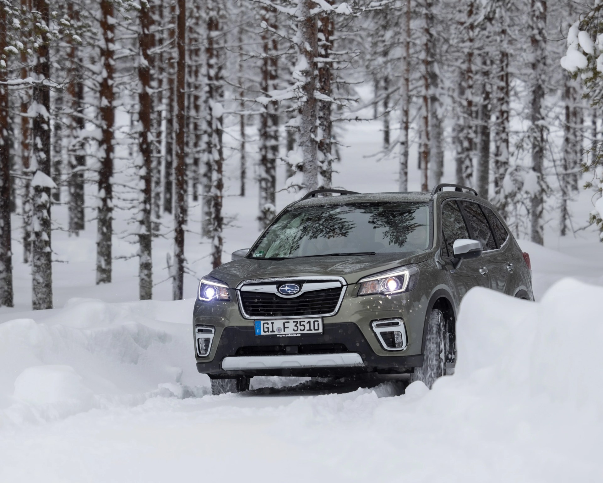 Green Subaru SUV driving on a snow-covered road in a snowy forest.