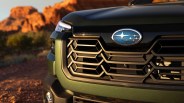 Front grille of a green Subaru vehicle with a blue Subaru logo and a rocky desert background.