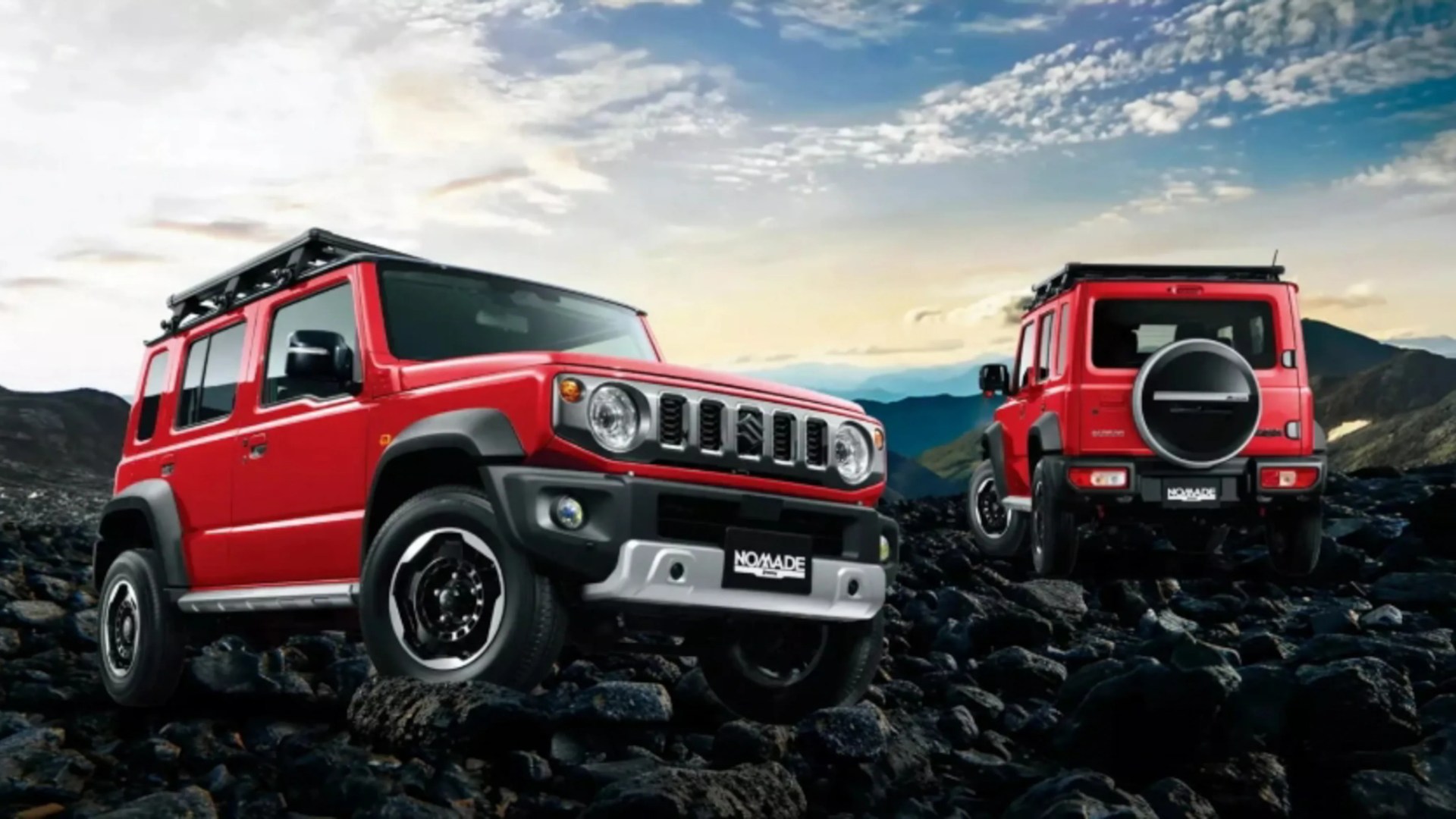 Two red Suzuki Jimny SUVs with roof racks parked on rocky terrain under a partly cloudy sky.