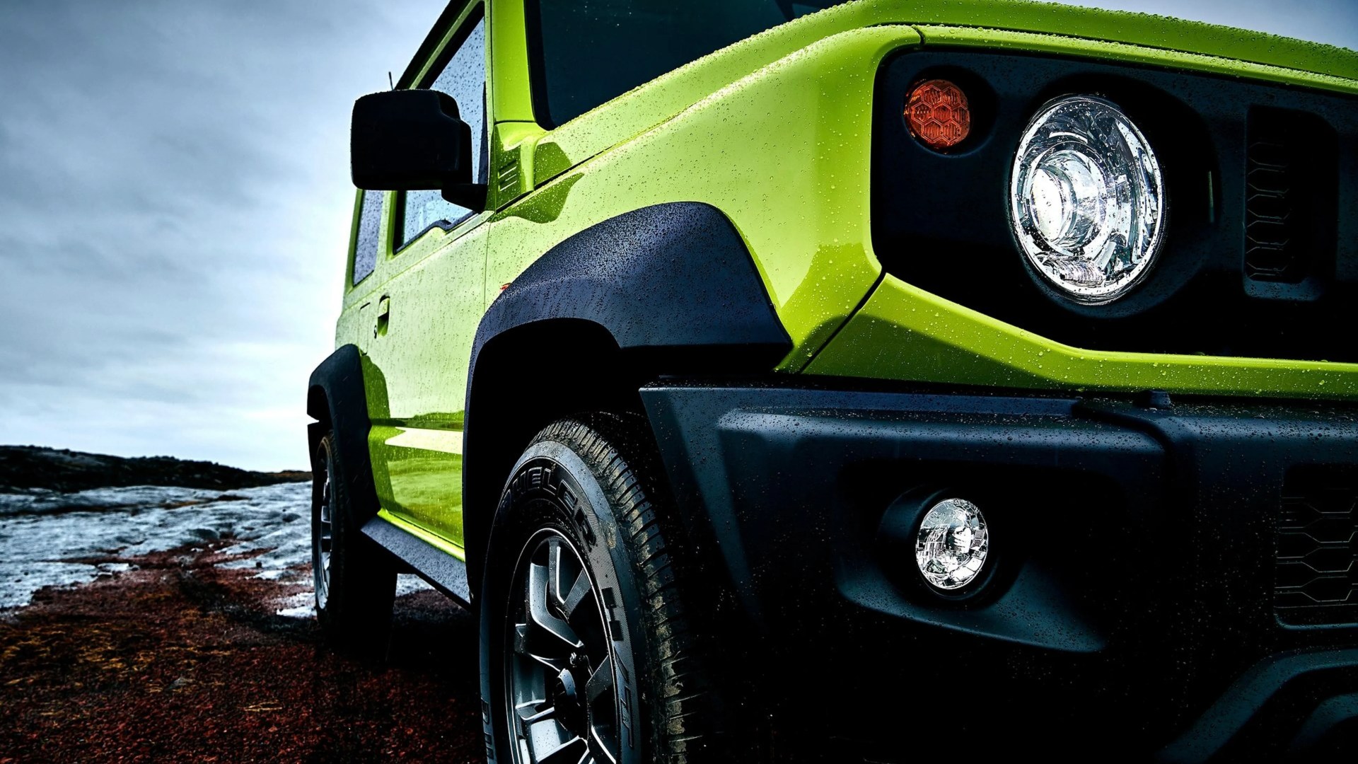 Bright green off-road vehicle with black fender flares and wet tires on muddy terrain.