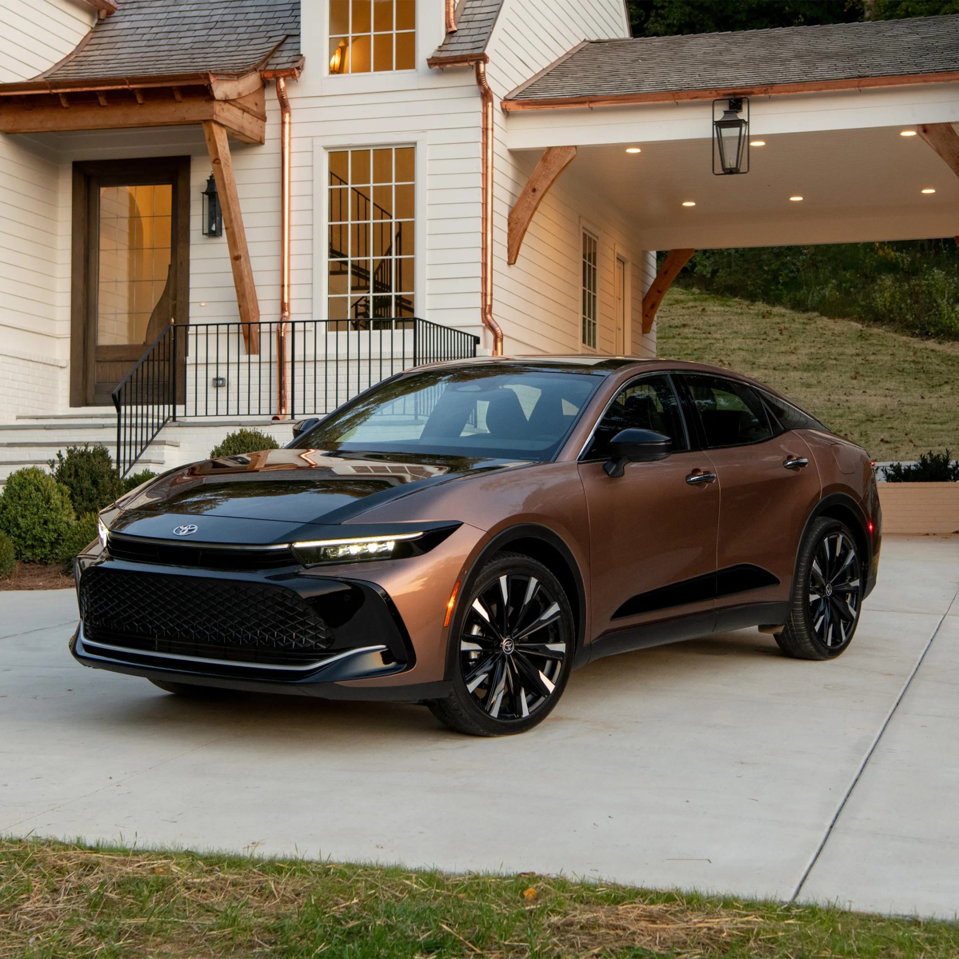 Bronze and black Toyota sedan parked on a driveway in front of a white house with copper gutters.