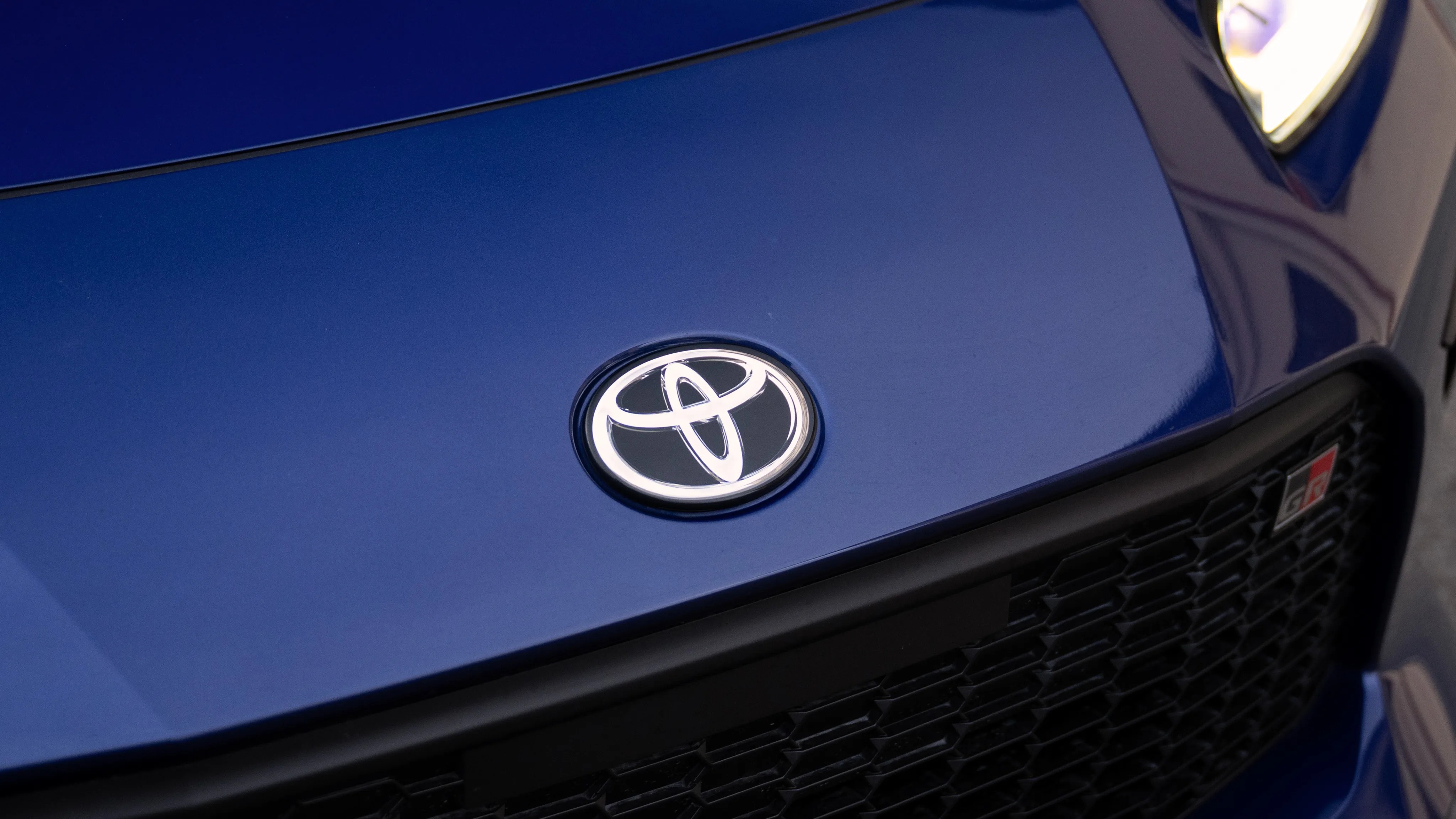 Glossy blue car hood with a silver Toyota emblem and a black grille featuring a red GR badge.