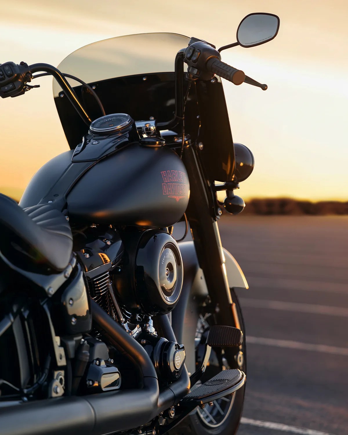 Black Harley-Davidson motorcycle with tinted windshield parked outdoors at sunset.