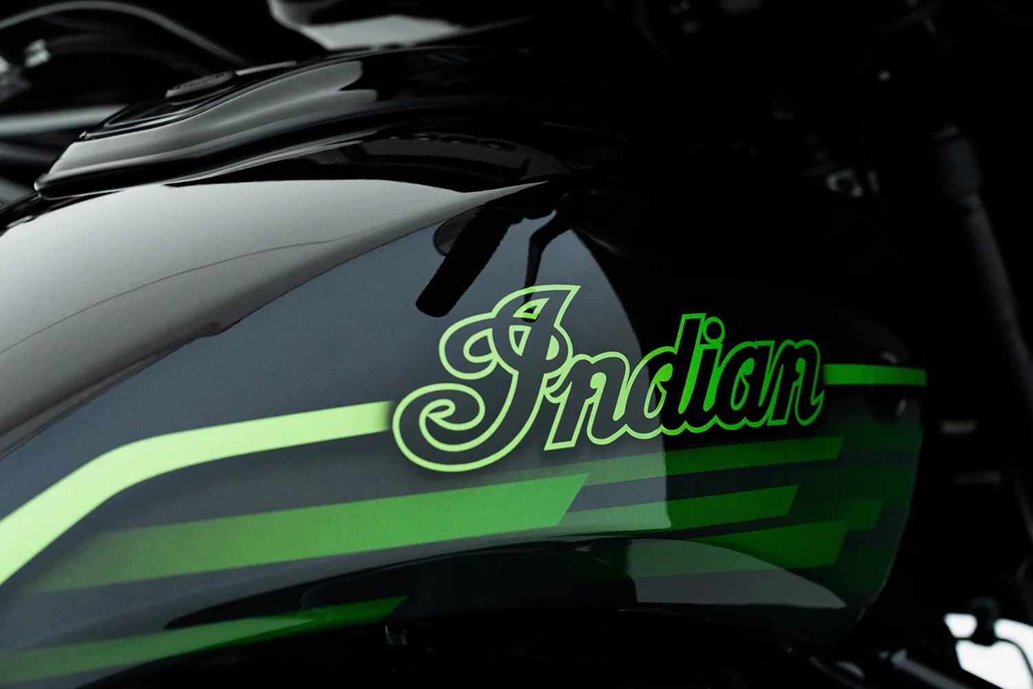 Glossy black motorcycle fuel tank with green stripes and "Indian" logo in green lettering.