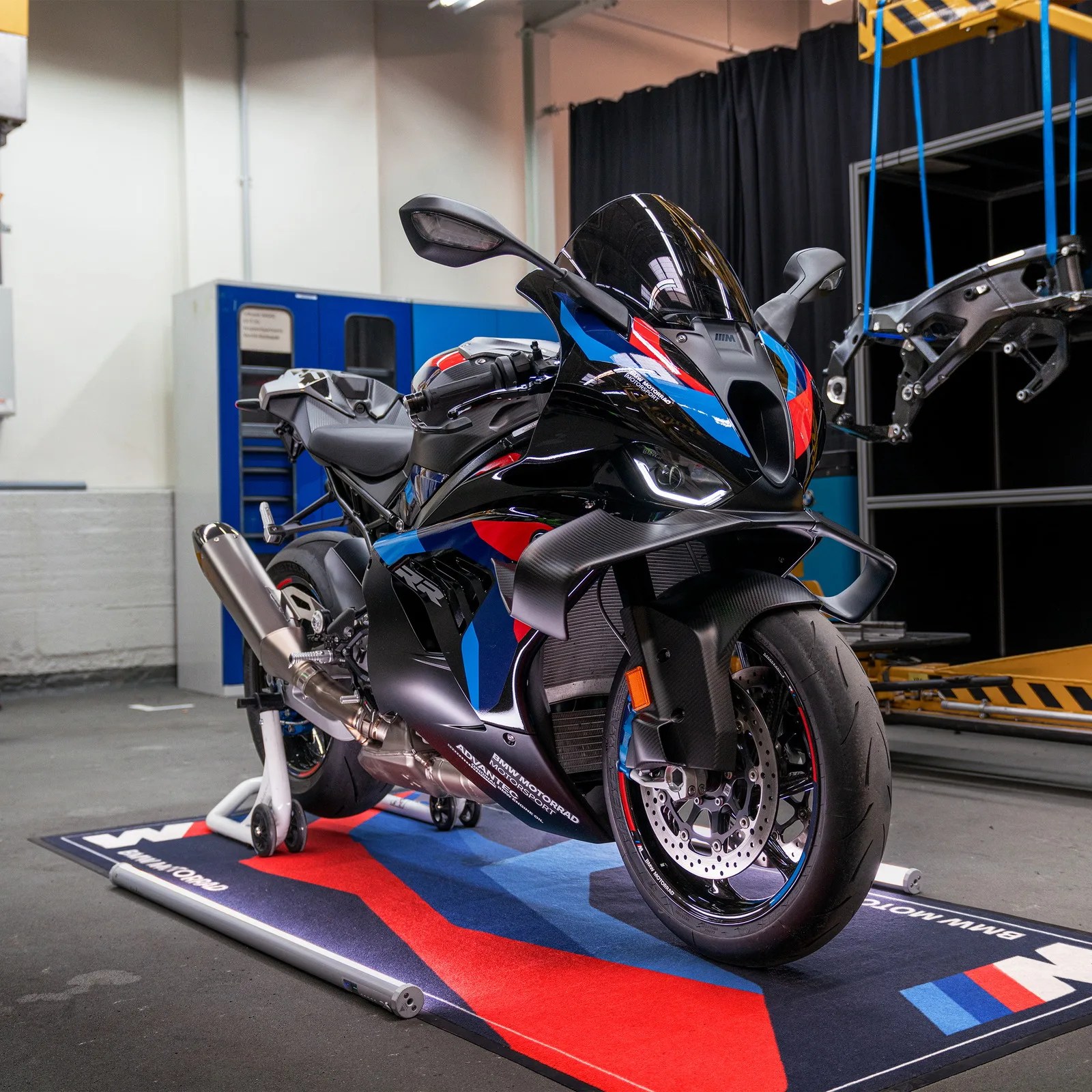 Black BMW sport motorcycle with blue and red accents on a BMW-branded mat in a workshop.