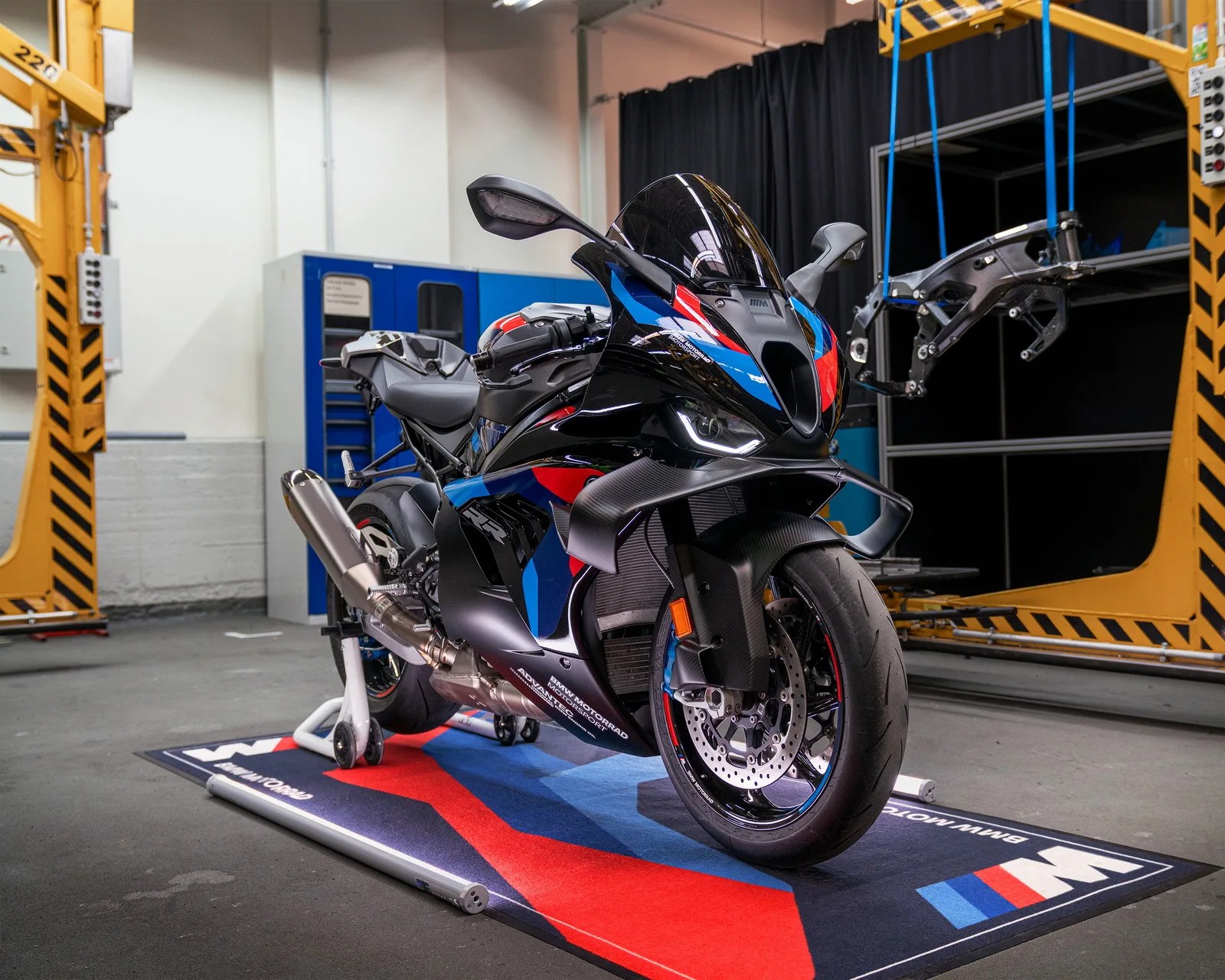 Black BMW sport motorcycle with blue and red accents on a BMW-branded mat in a workshop.