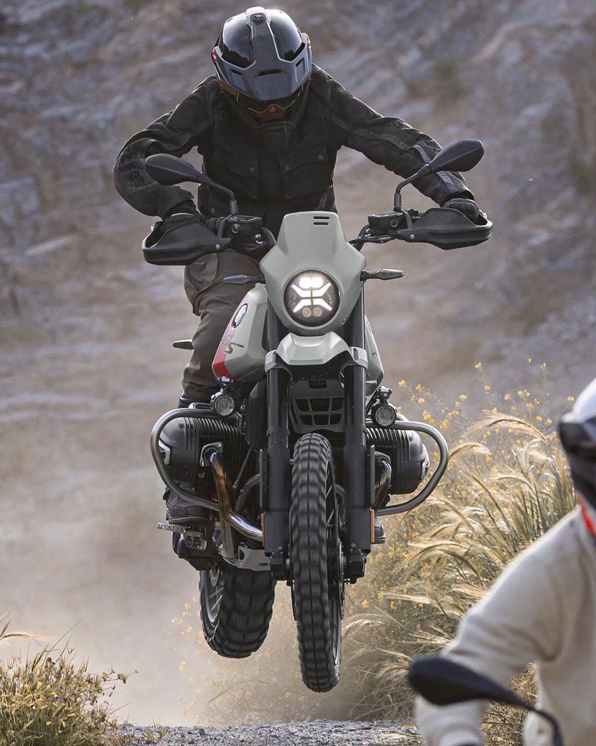Motorcyclist wearing a black helmet and jacket riding a white BMW GS motorcycle off-road with front wheel lifted.