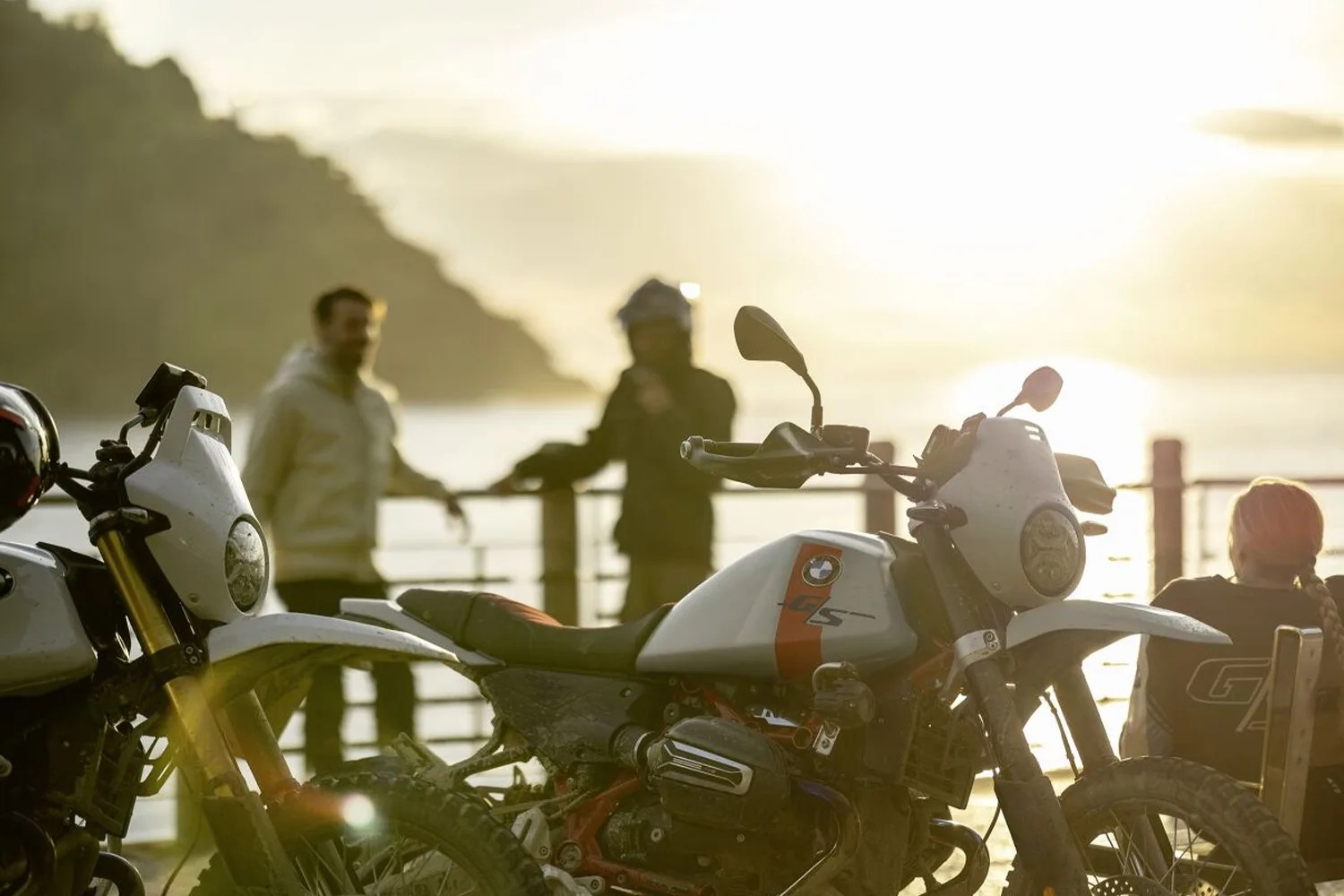 White BMW GS adventure motorcycle with off-road tires parked near a waterfront at sunset.