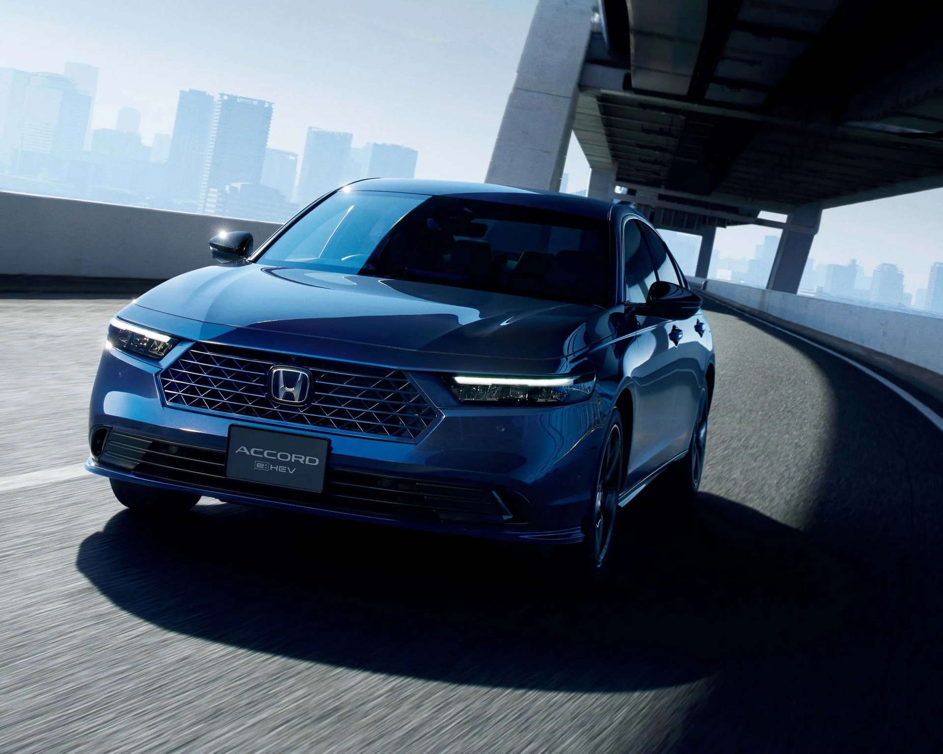 Blue Honda Accord e:HEV sedan driving on a curved elevated road with city skyline in the background.