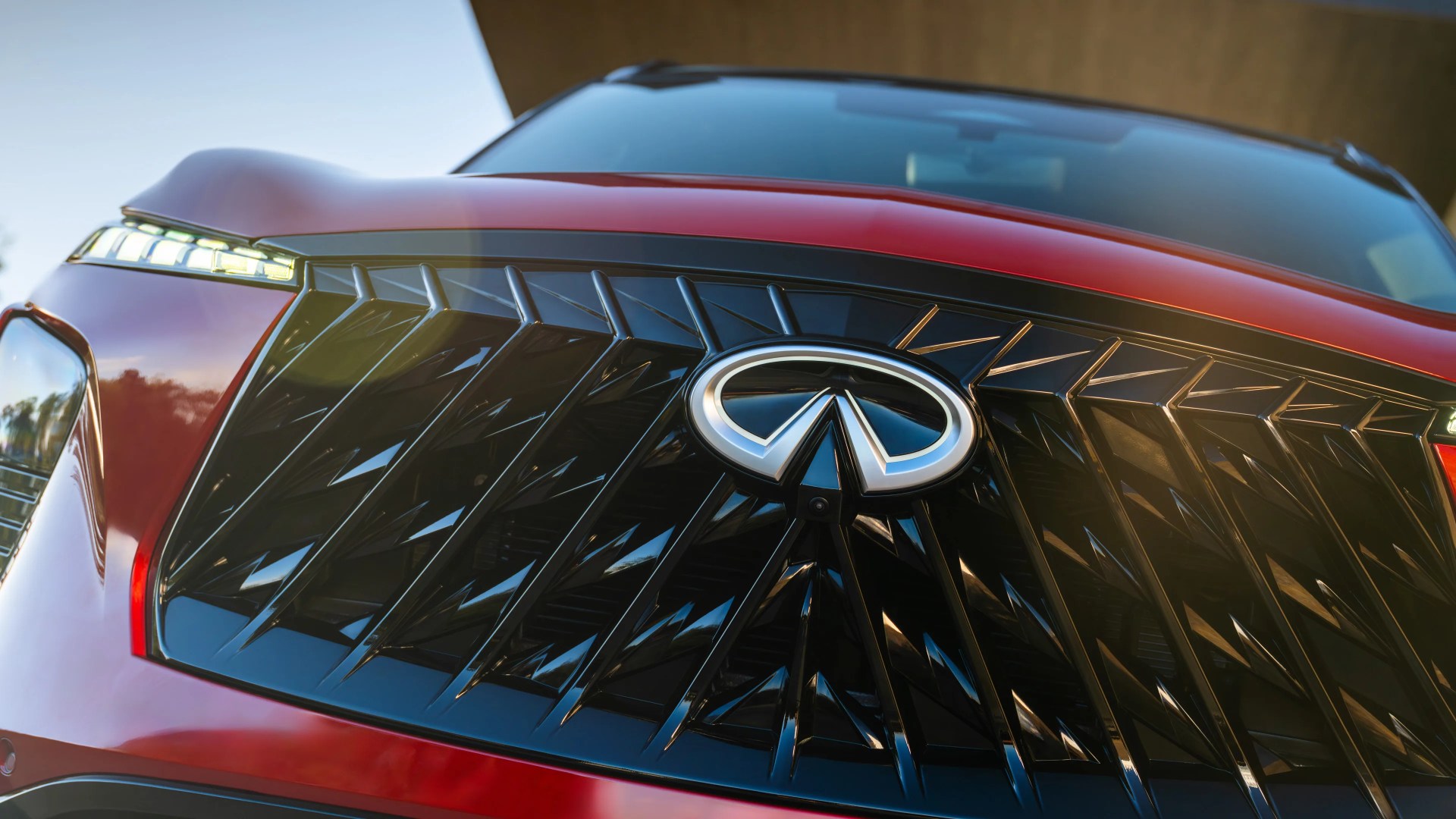 Close-up of a red car front grille with a black geometric pattern and an Infiniti logo in the center.