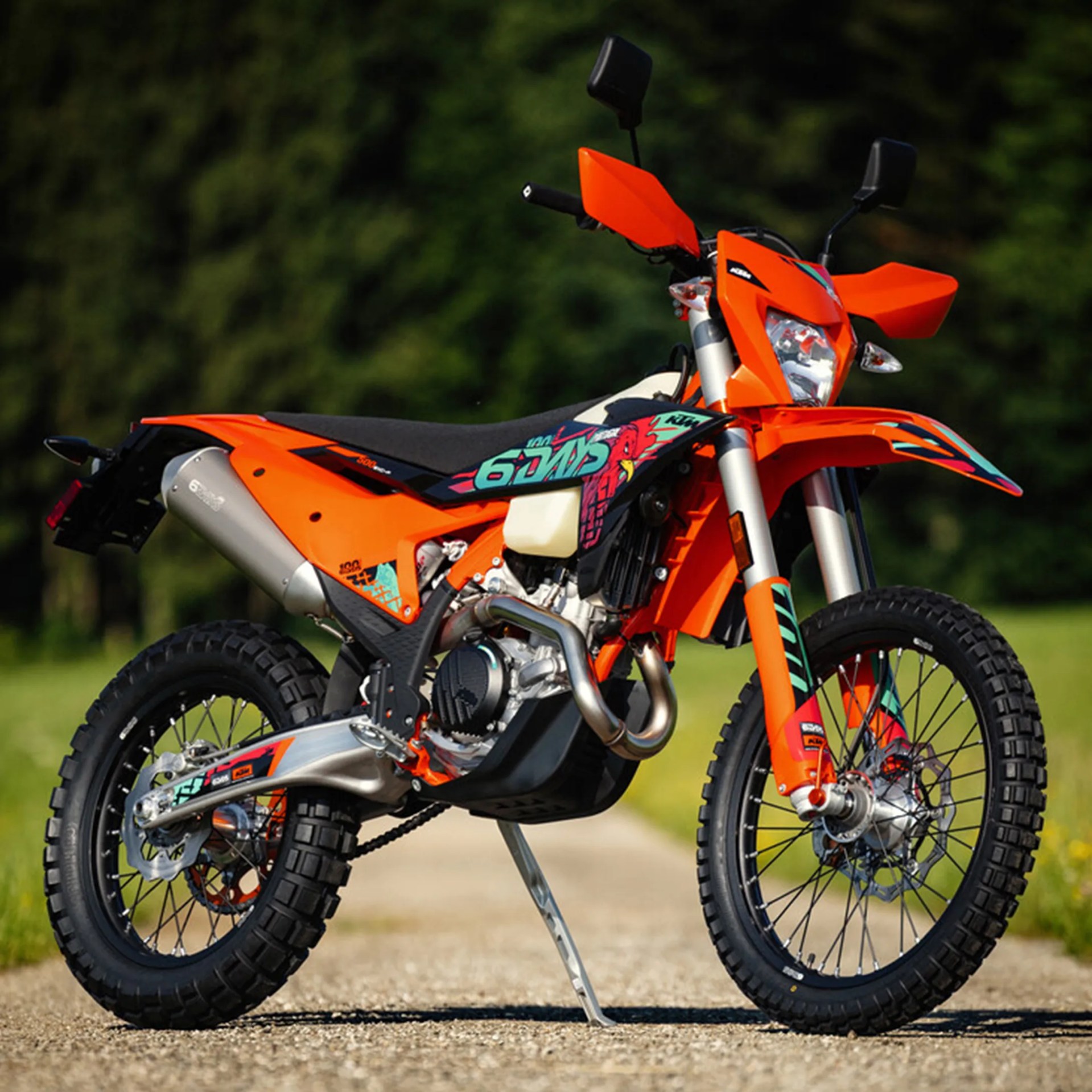 Orange KTM off-road motorcycle with knobby tires and colorful decals on a gravel path.