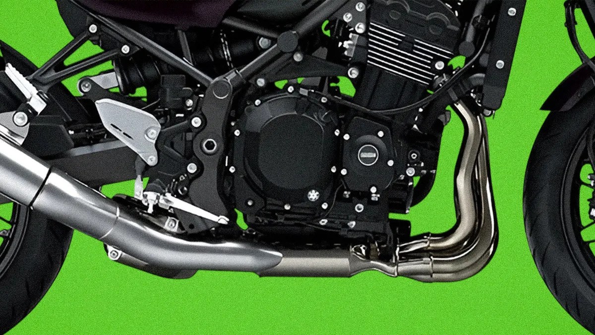 Close-up of a motorcycle engine and exhaust system with black and silver components against a green background.