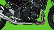 Close-up of a motorcycle engine and exhaust system with black and silver components against a green background.