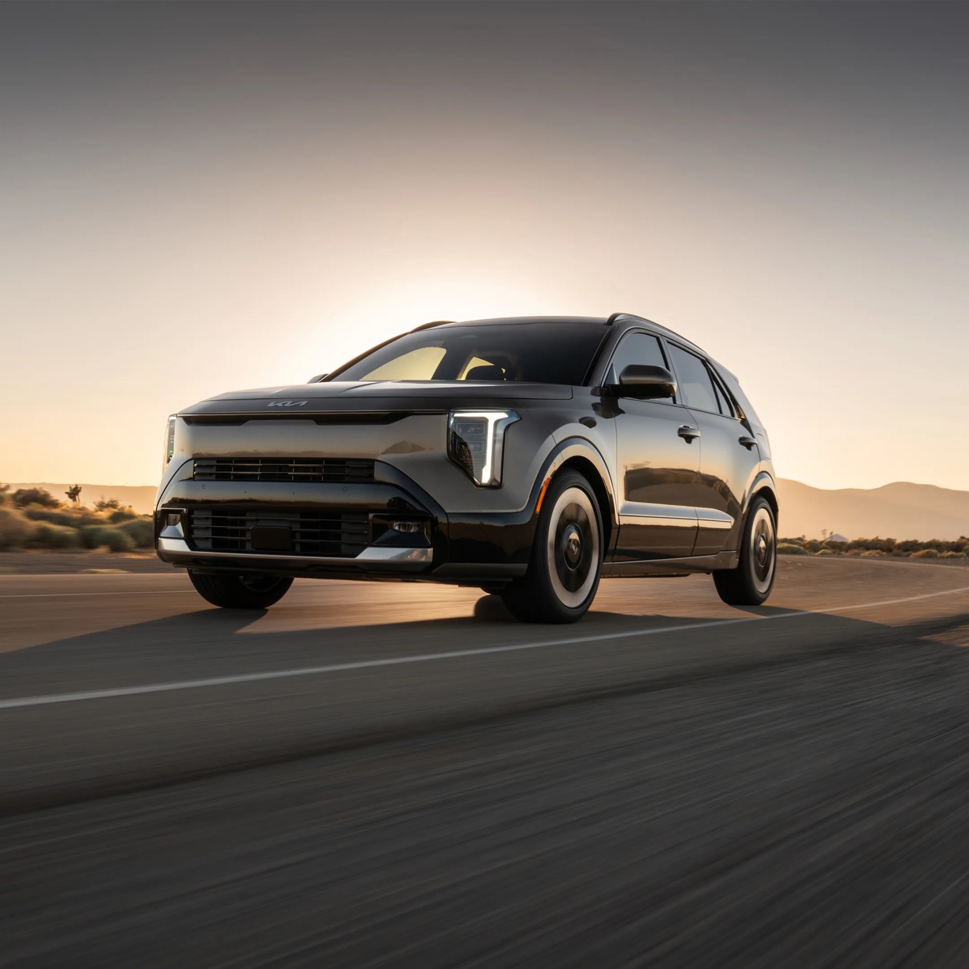 Black Kia SUV with LED headlights driving on a road at sunset.