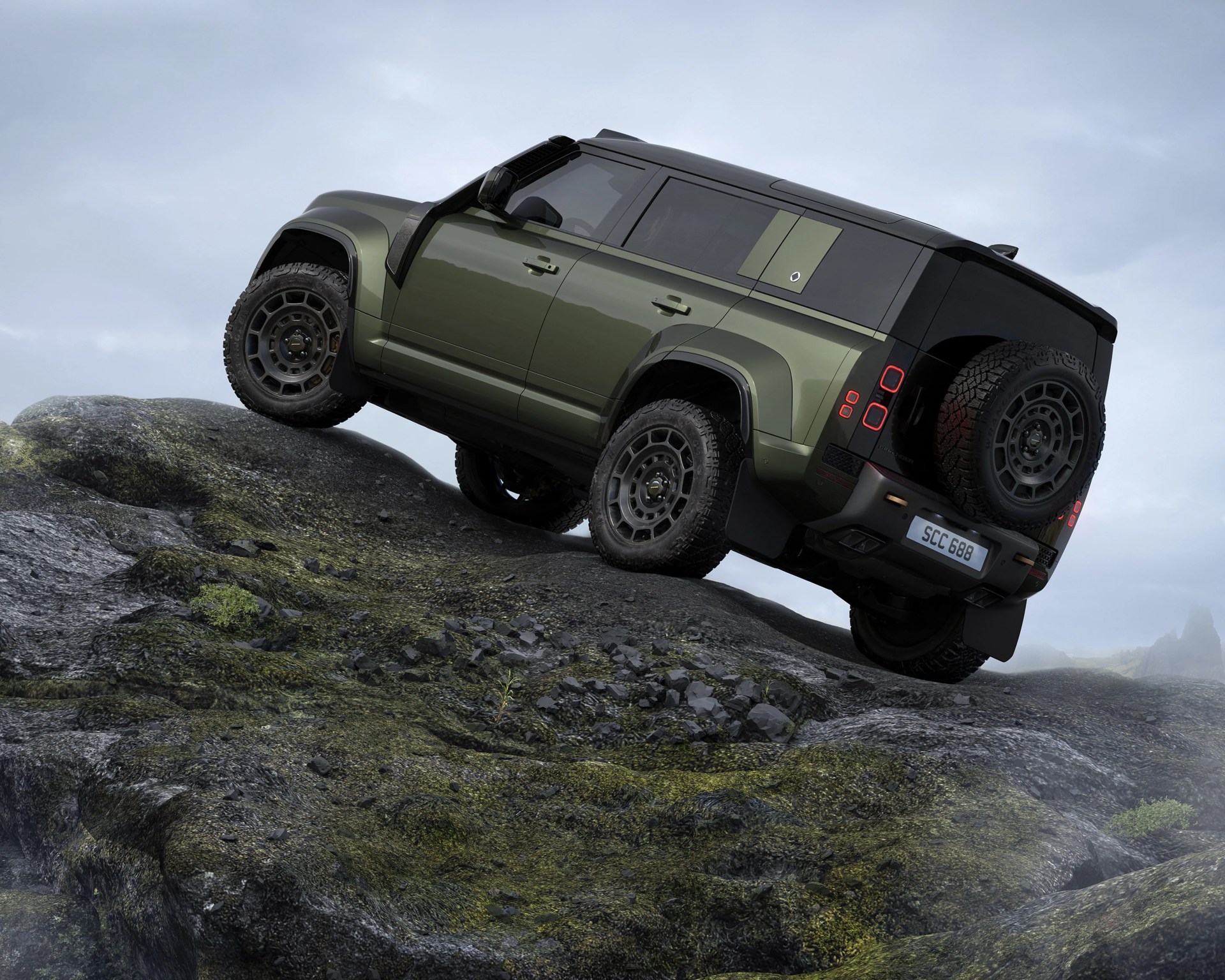 Green and black off-road SUV climbing a rocky hill under a cloudy sky.