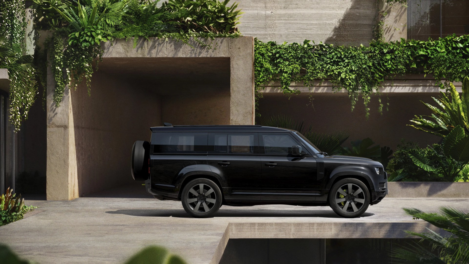 Black modern SUV parked on a concrete driveway with green plants and vines on a stone wall.