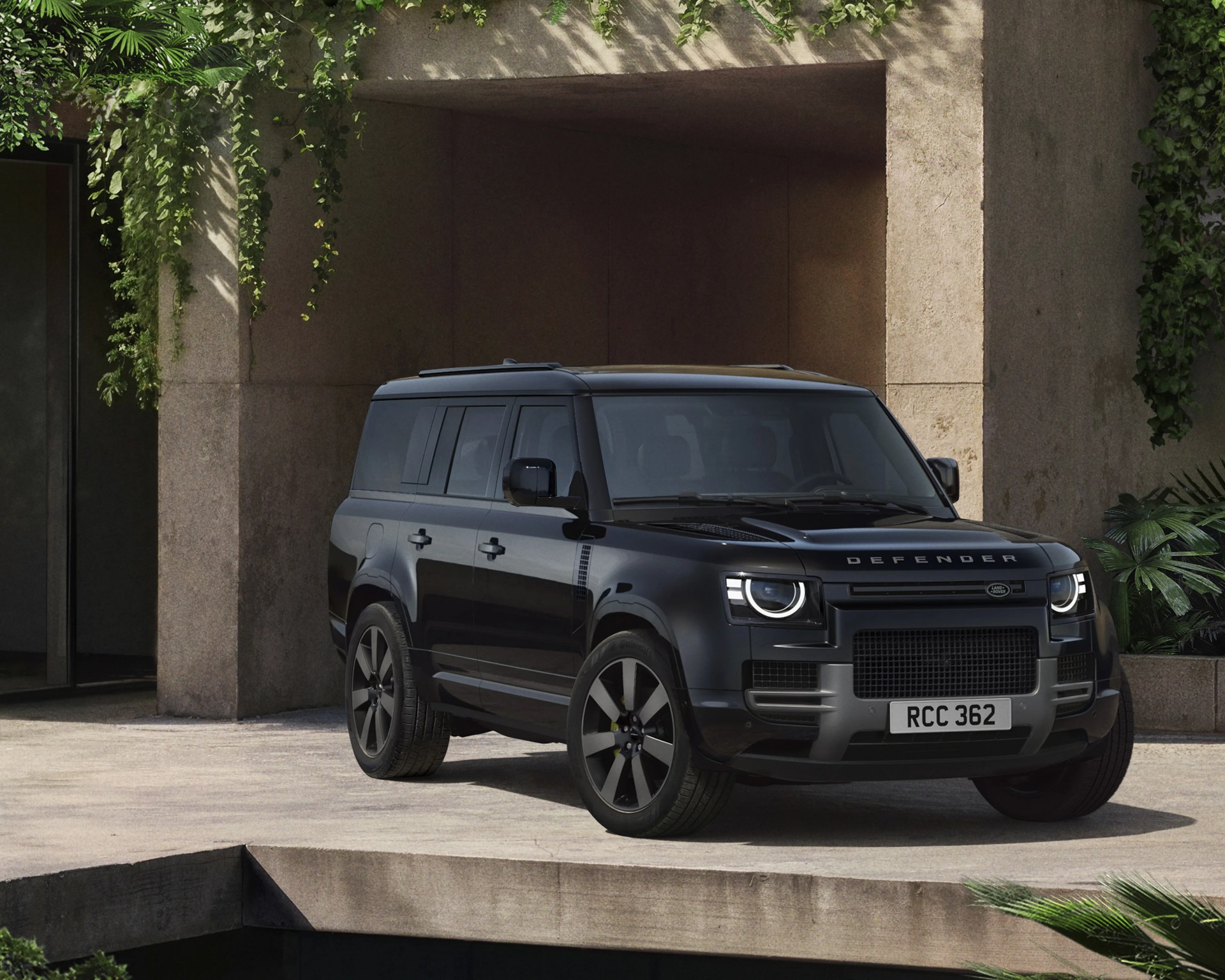 Black Land Rover Defender SUV parked on a concrete driveway next to a building with hanging greenery.
