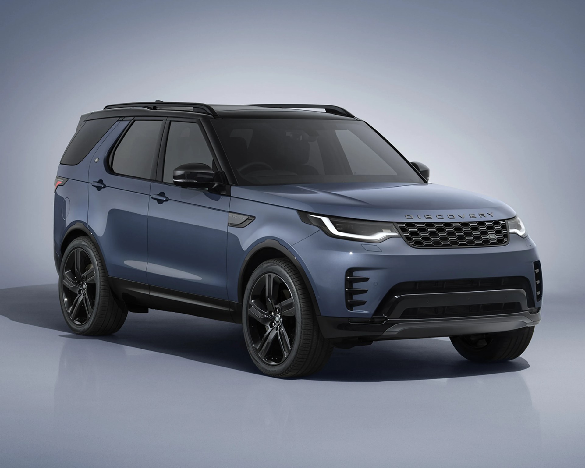 Blue Land Rover Discovery SUV with black roof and black wheels on a gray reflective floor.