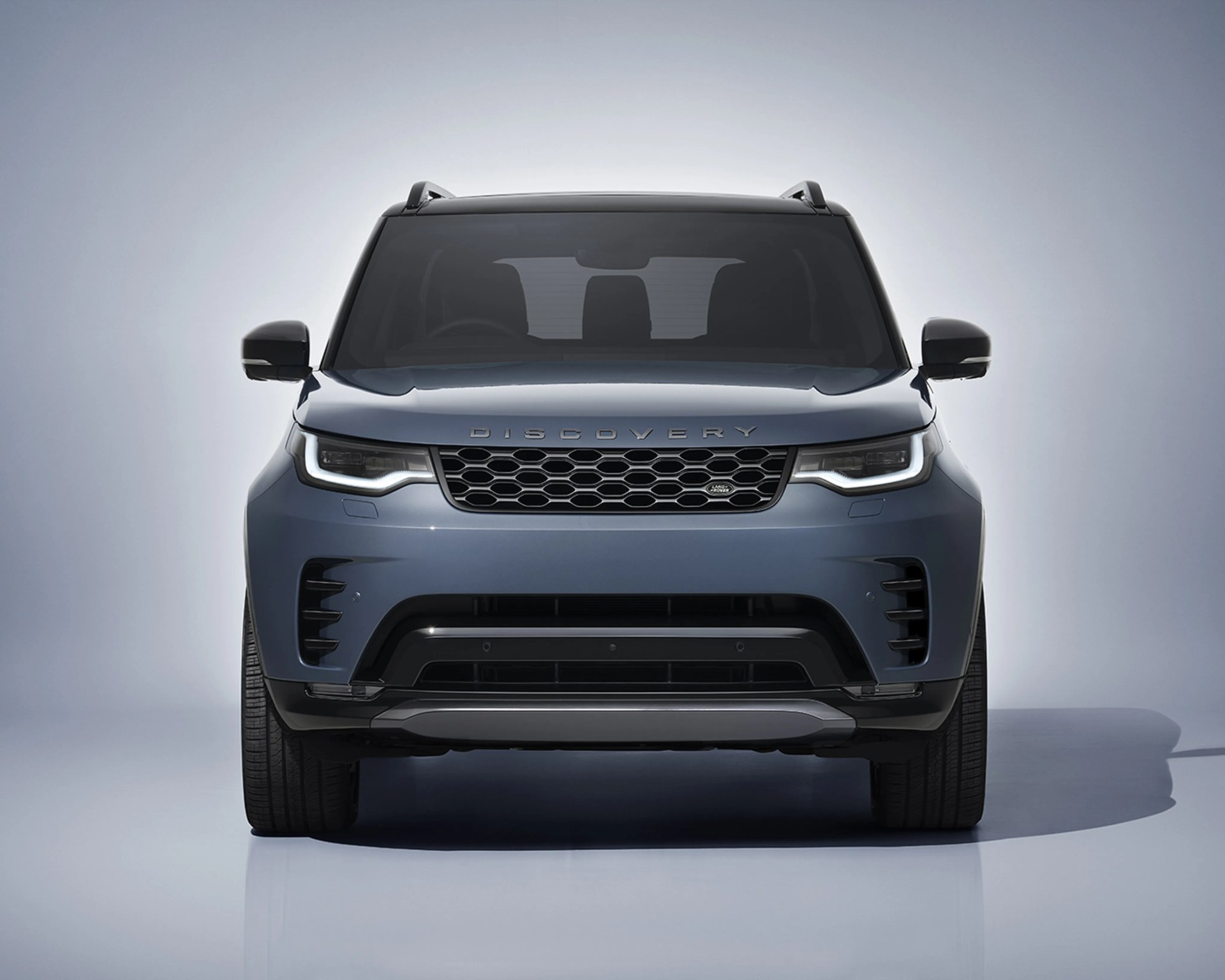 Front view of a blue Land Rover Discovery with LED headlights and black grille on a light gray background.