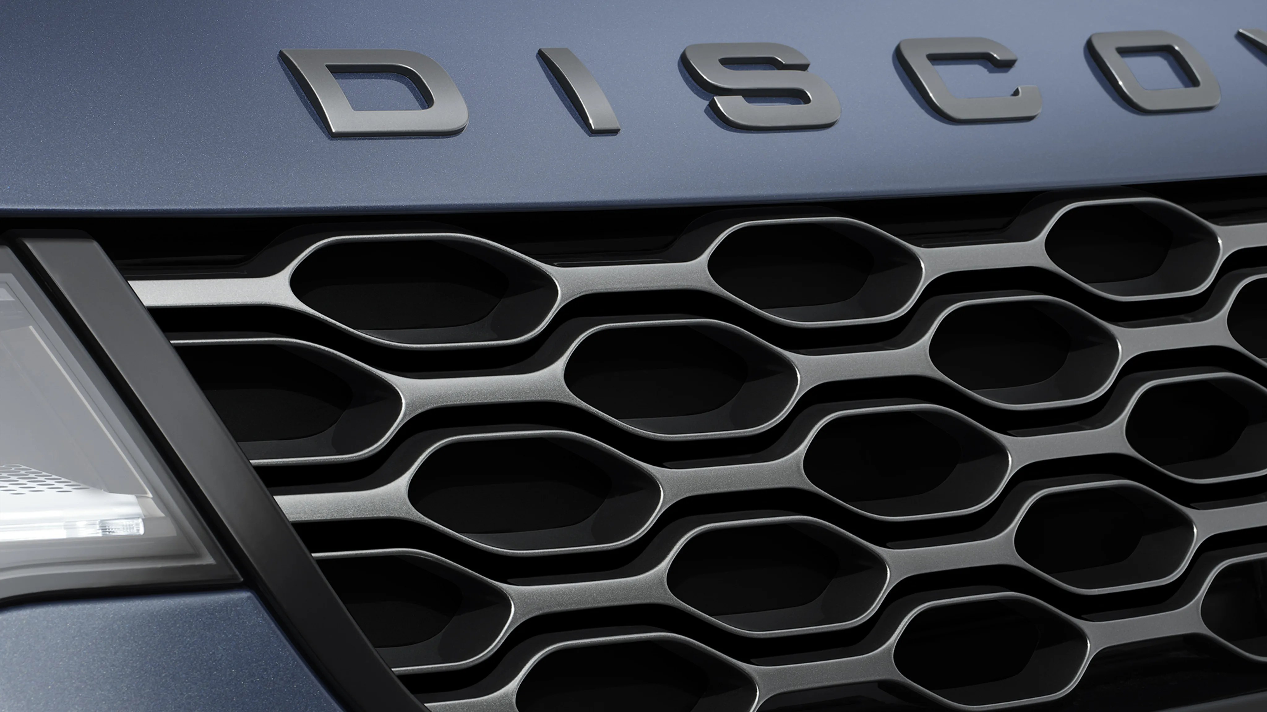 Close-up of a blue Land Rover Discovery front grille with honeycomb pattern and partial headlight.