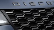 Close-up of a blue Land Rover Discovery front grille with honeycomb pattern and partial headlight.