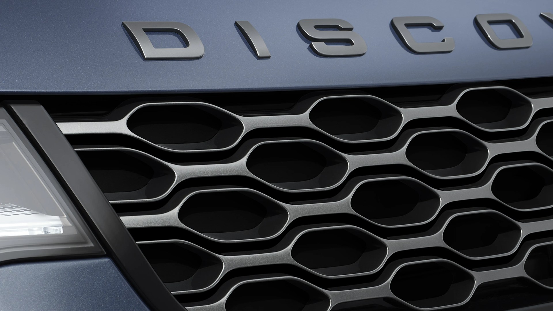 Close-up of a blue Land Rover Discovery front grille with honeycomb pattern and partial headlight.