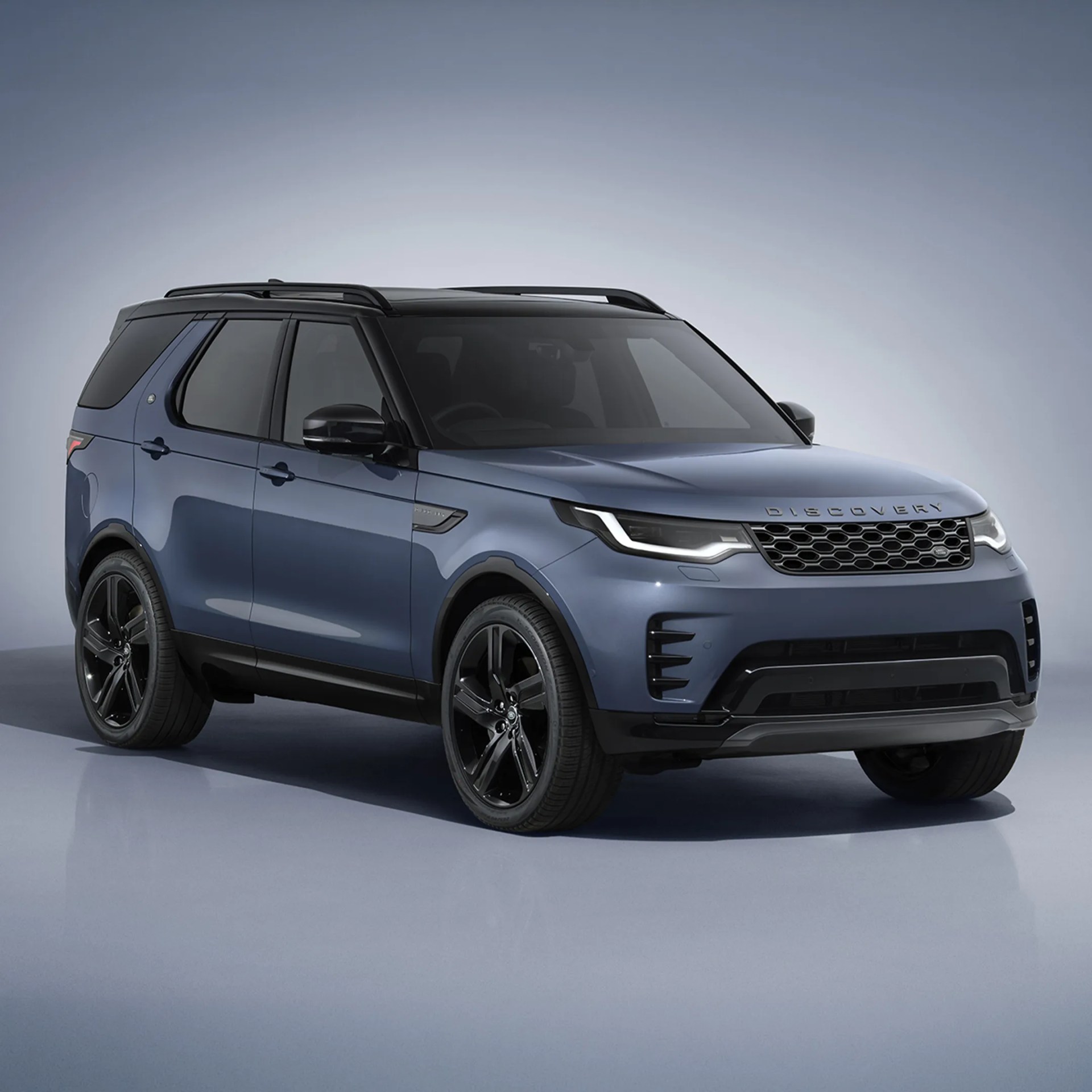 Blue Land Rover Discovery SUV with black roof rails and black alloy wheels on a reflective surface.