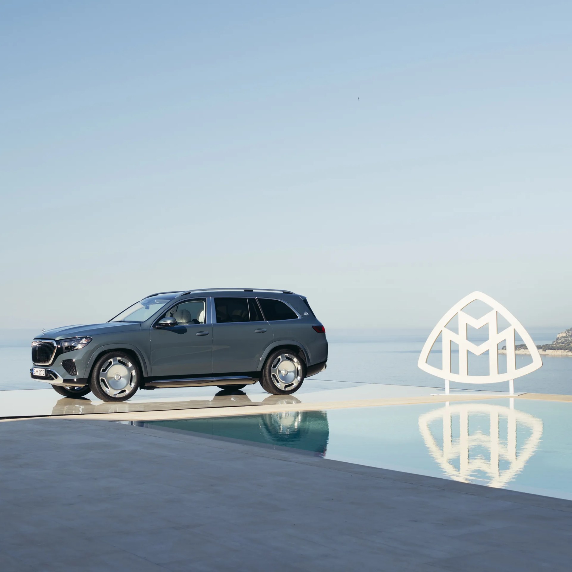 Dark gray Mercedes-Maybach GLS SUV parked beside a pool with a large Maybach logo sculpture nearby.