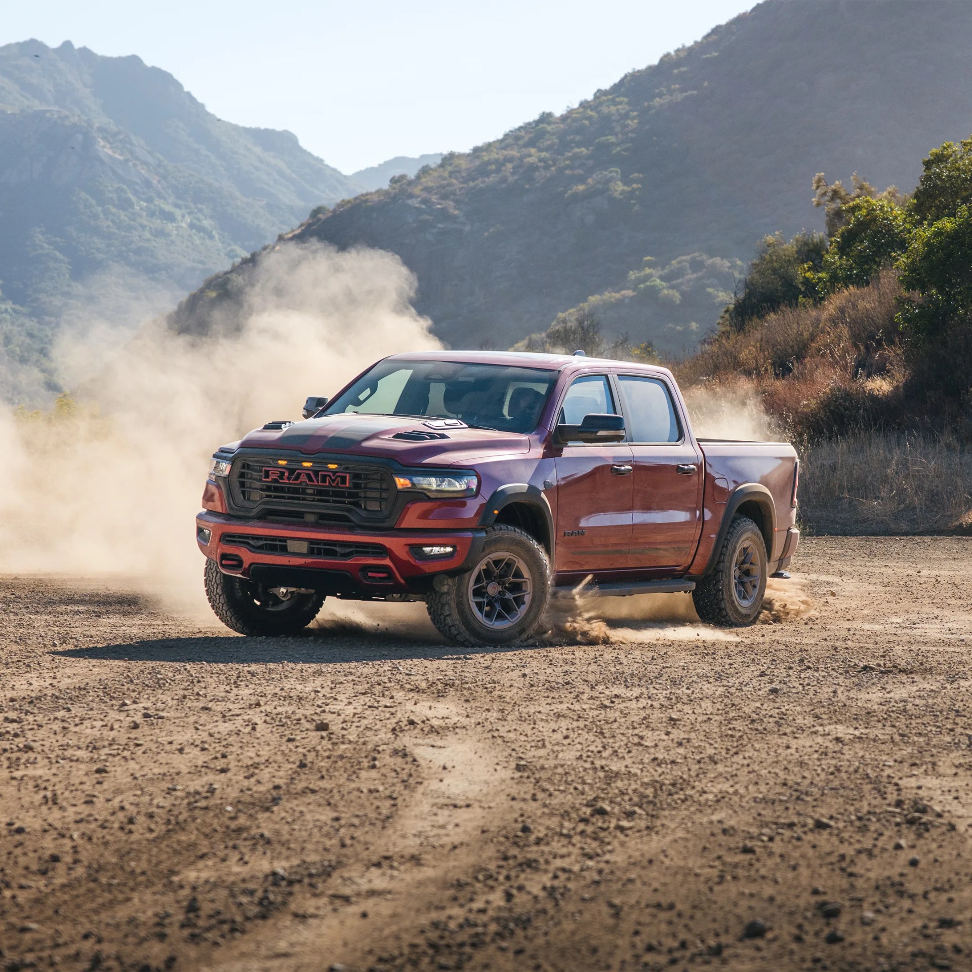 Red RAM pickup truck kicking up dust on a dirt road with mountains in the background.