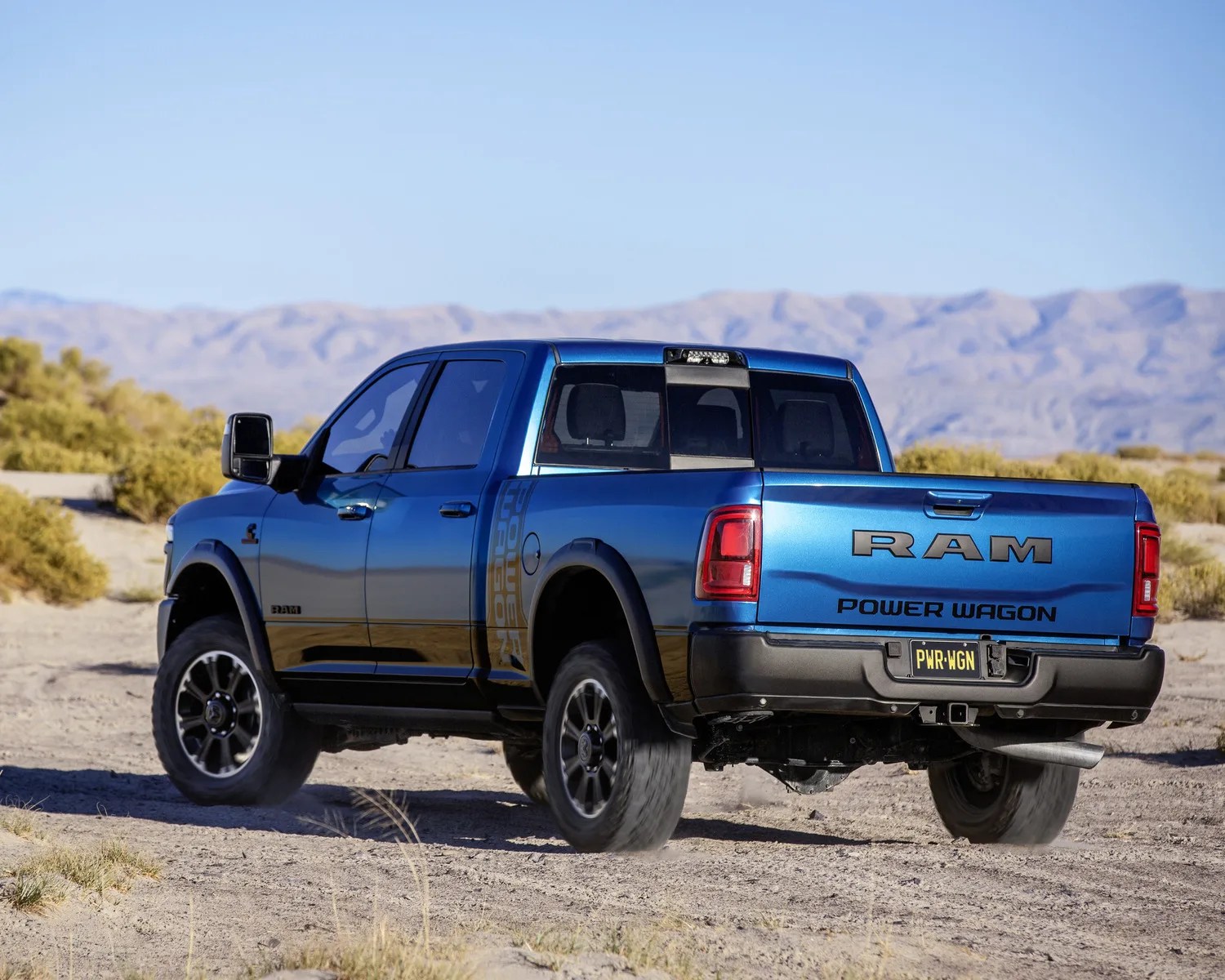 Blue RAM Power Wagon pickup truck driving on a dirt road with mountains in the background.