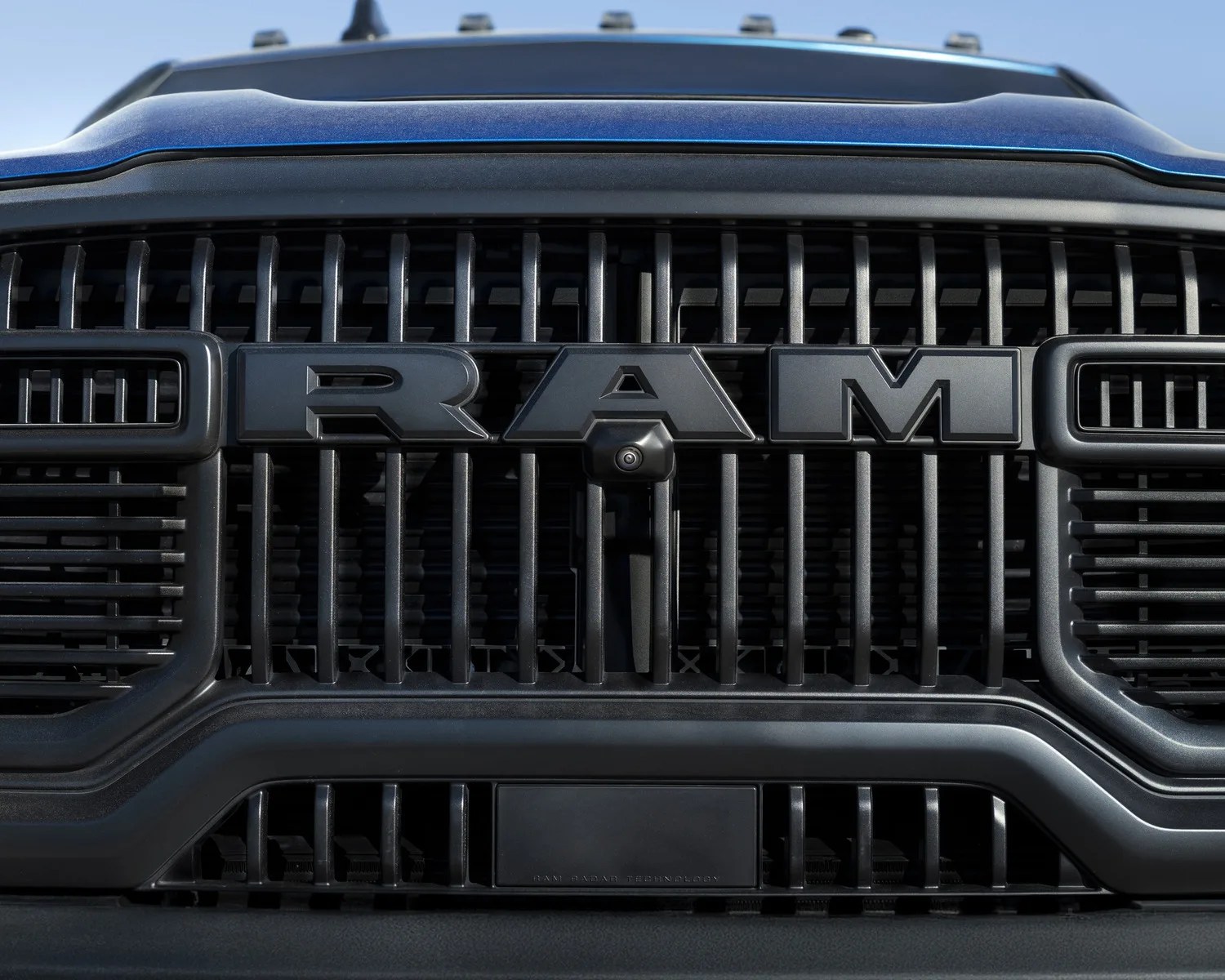 Close-up of a black RAM truck grille with bold RAM lettering and a front-facing camera.