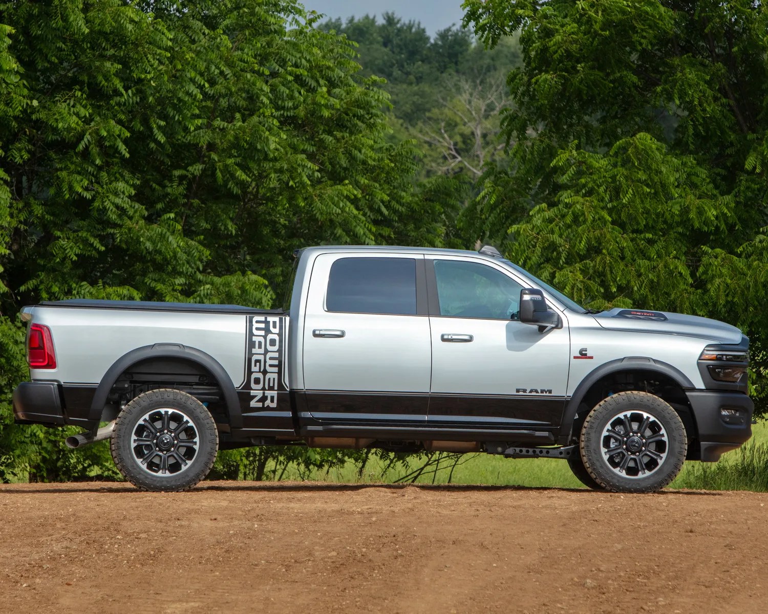 Silver and black Ram Power Wagon pickup truck parked on dirt with green trees in the background.